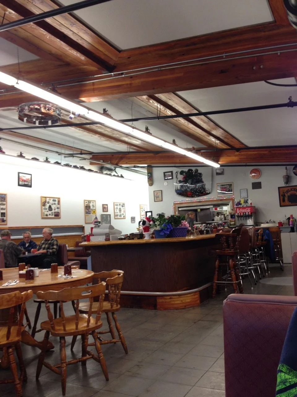 Inside a restaurant with booths, tables, and a bar area, decorated with pictures and memorabilia on the walls, with several customers and staff present.