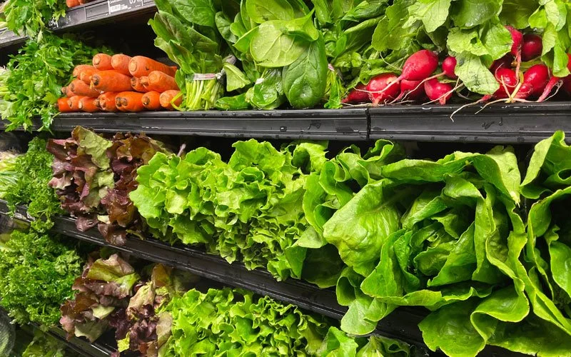 Fresh carrots, spinach, radishes, and various leafy greens on store shelves.