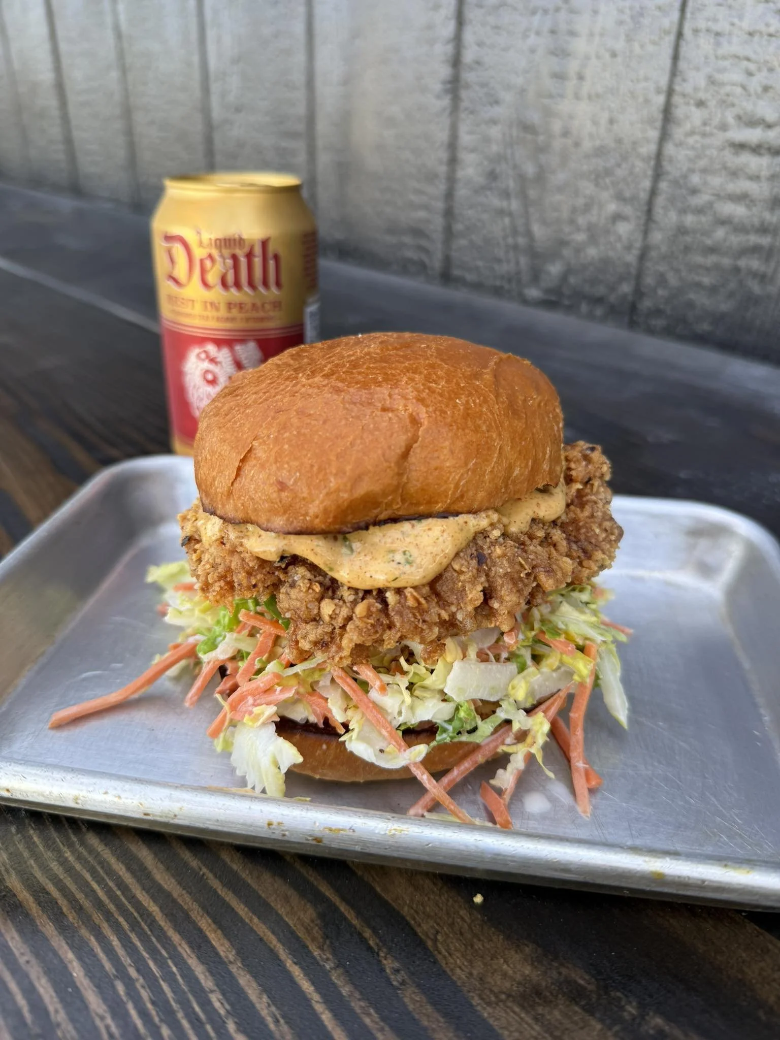 Fried chicken sandwich with lettuce, coleslaw, and sauce in a bun with a Death Water behind it