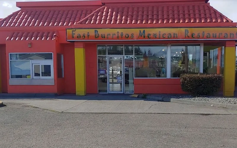 Exterior of a Mexican restaurant called Fast Burritos, with a red tiled roof, red walls, and large front windows, located in a shopping area.