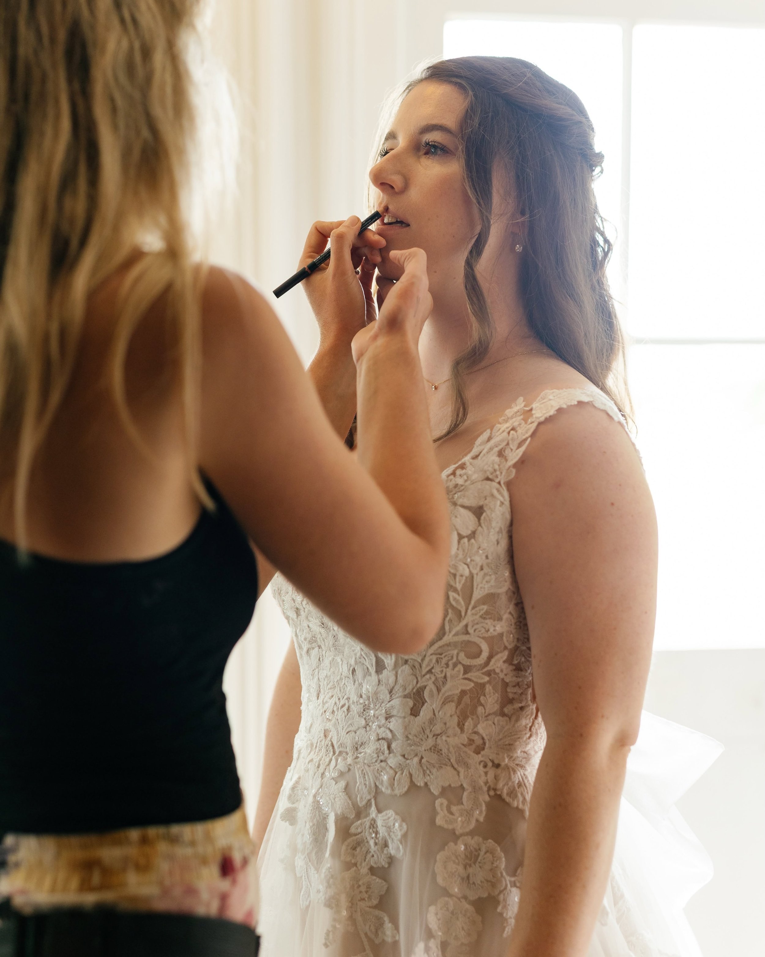 A beautician putting on wedding makeup on a bride.