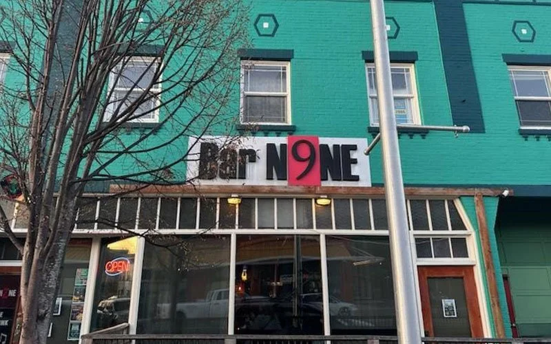 Storefront with sign reading 'BOOK NINE' with the letter '9' in red, on a teal building with windows and a small tree in front.