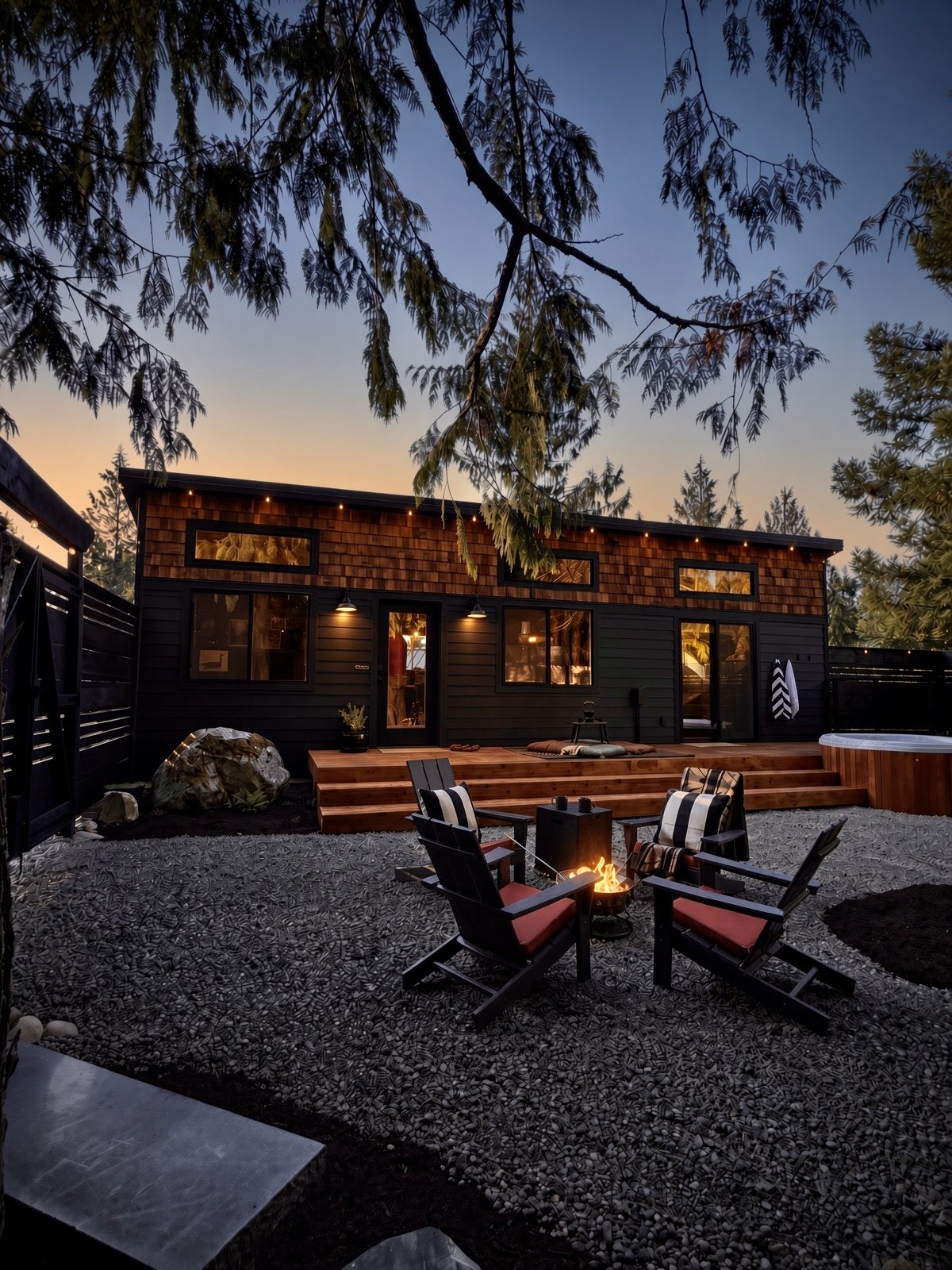 The outside of The Sugi Box Air Bnb in Port Angeles, featuring a charcoal-colored and wood decorated tiny home with a firepit seating area outside.