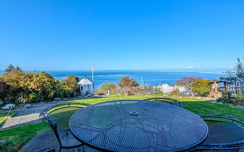 Outdoor patio table overlooking a garden and ocean view with clear blue sky.