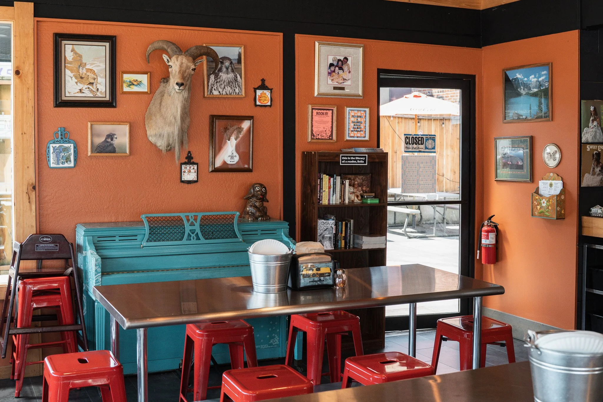 Inside the parlor of Dead Low Pizza, with terra cotta painted walls with various artwork, cast iron paddles, and a goat head mount.