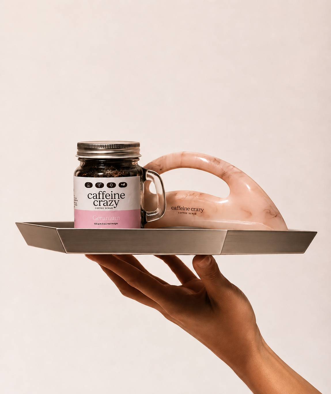 Geranium coffee scrub and gua sha body sculpt tool served on a silver platter.