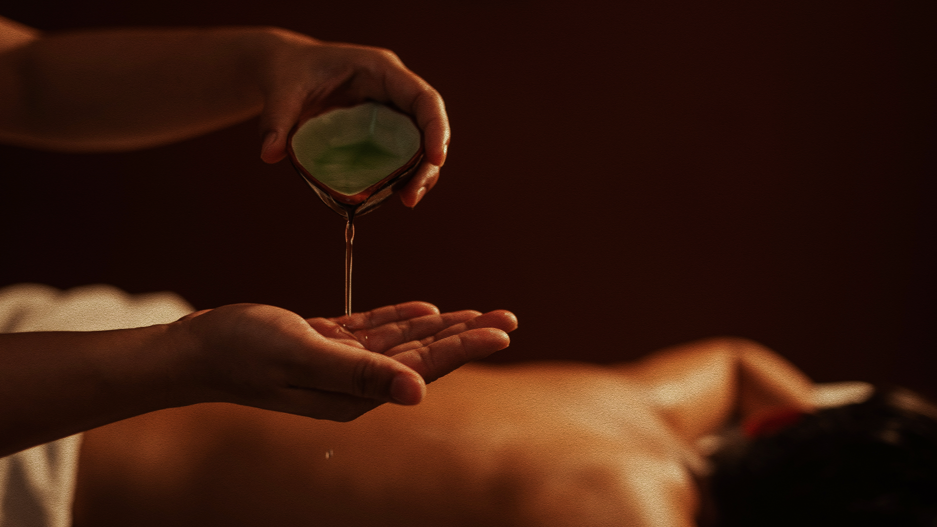 massage therapist pours oil onto hand to prepare for use on client’s back