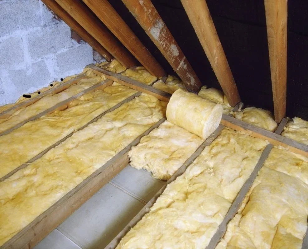 Insulation being installed in an attic space, with yellow fiberglass insulation and wooden rafters.
