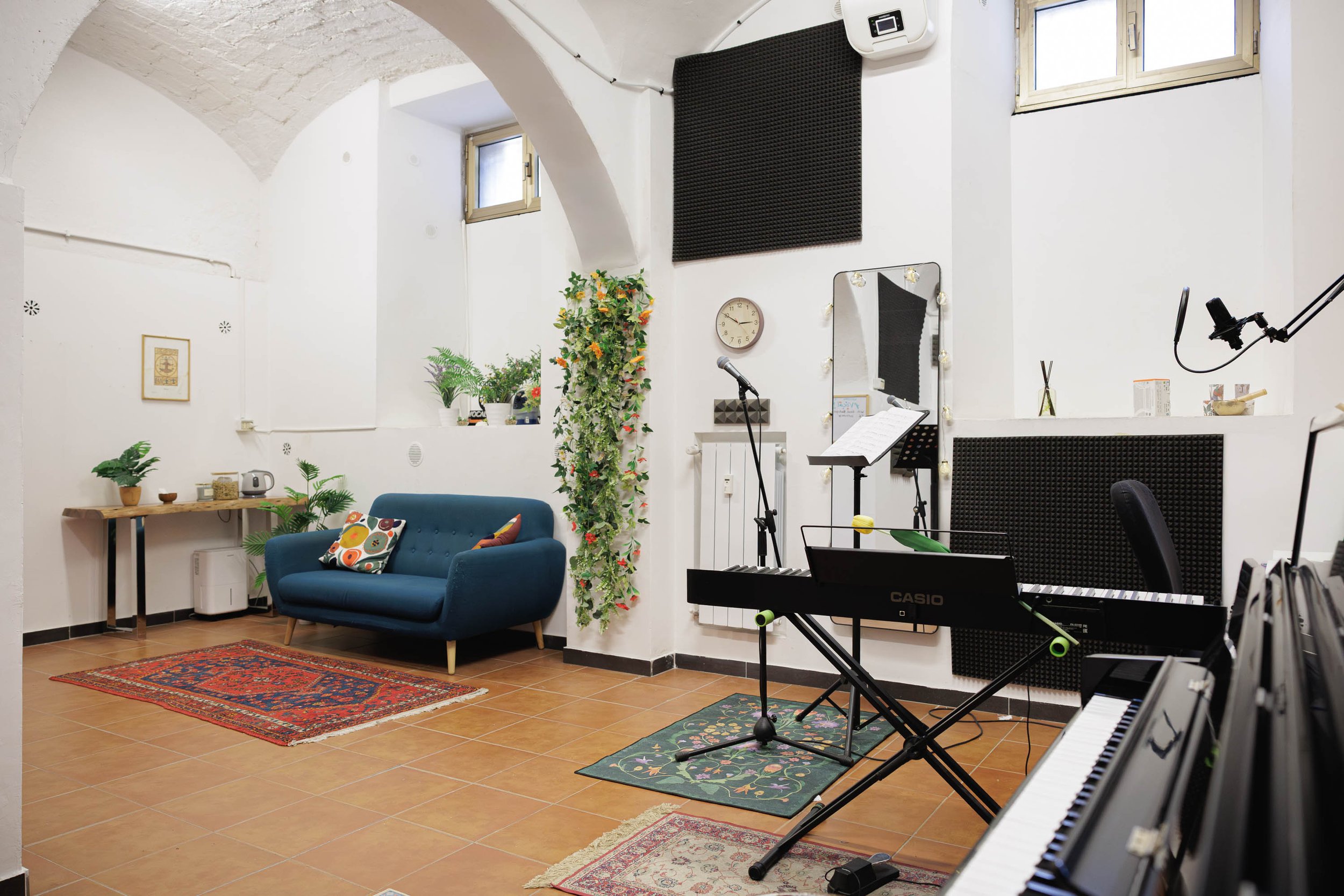 Stanza di prova o sala di musica con divano blu, piante, microfono, tastiere e poltrona