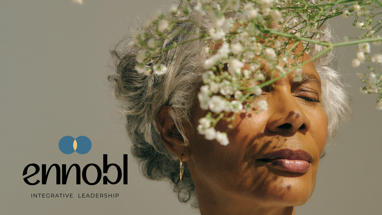 Woman with serene expression standing behind flowers.