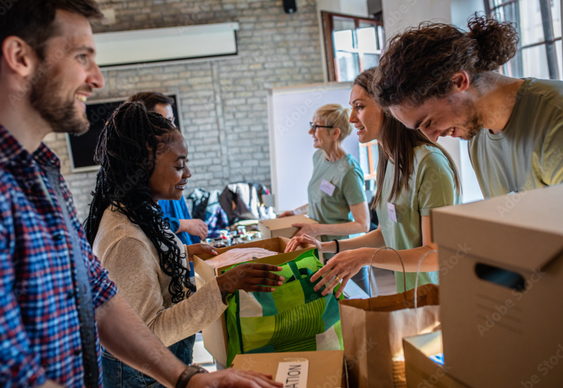 People smiling and exchanging items at a charity donation event inside a room.