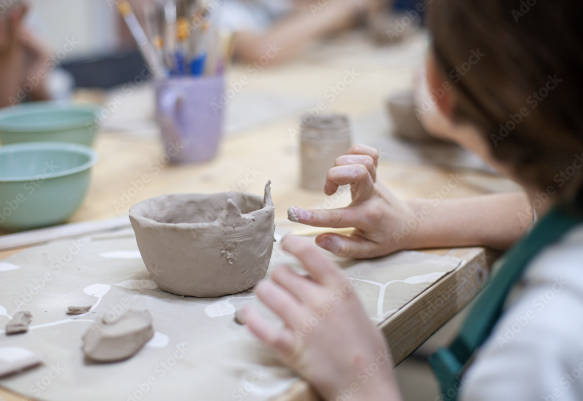 Child shaping a clay pot at a pottery workshop with pottery tools, bowls, and art supplies on the table.