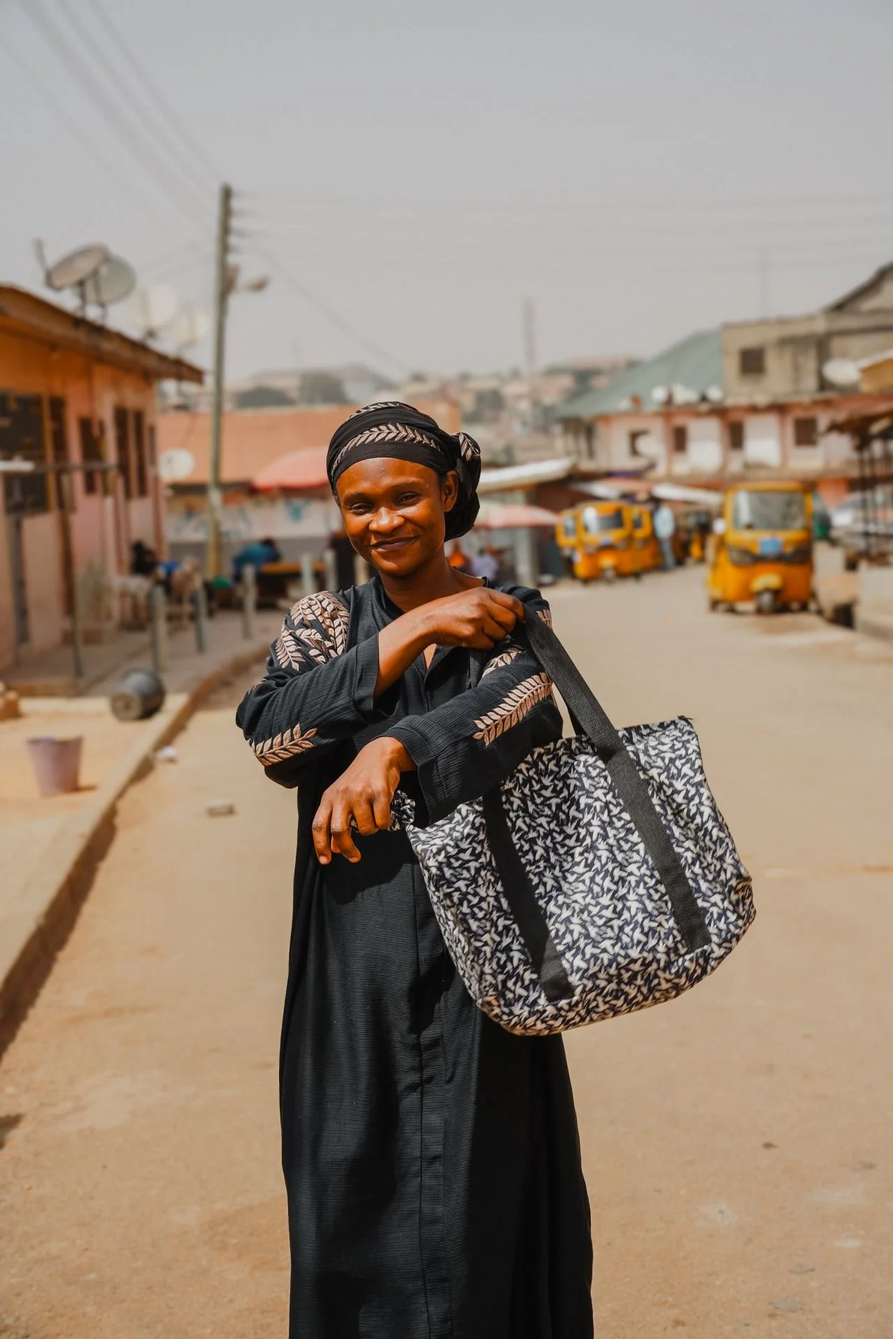 Seamstress stands in the streets of Kumasi, proudly holding an upcycled bag with blue and white print.