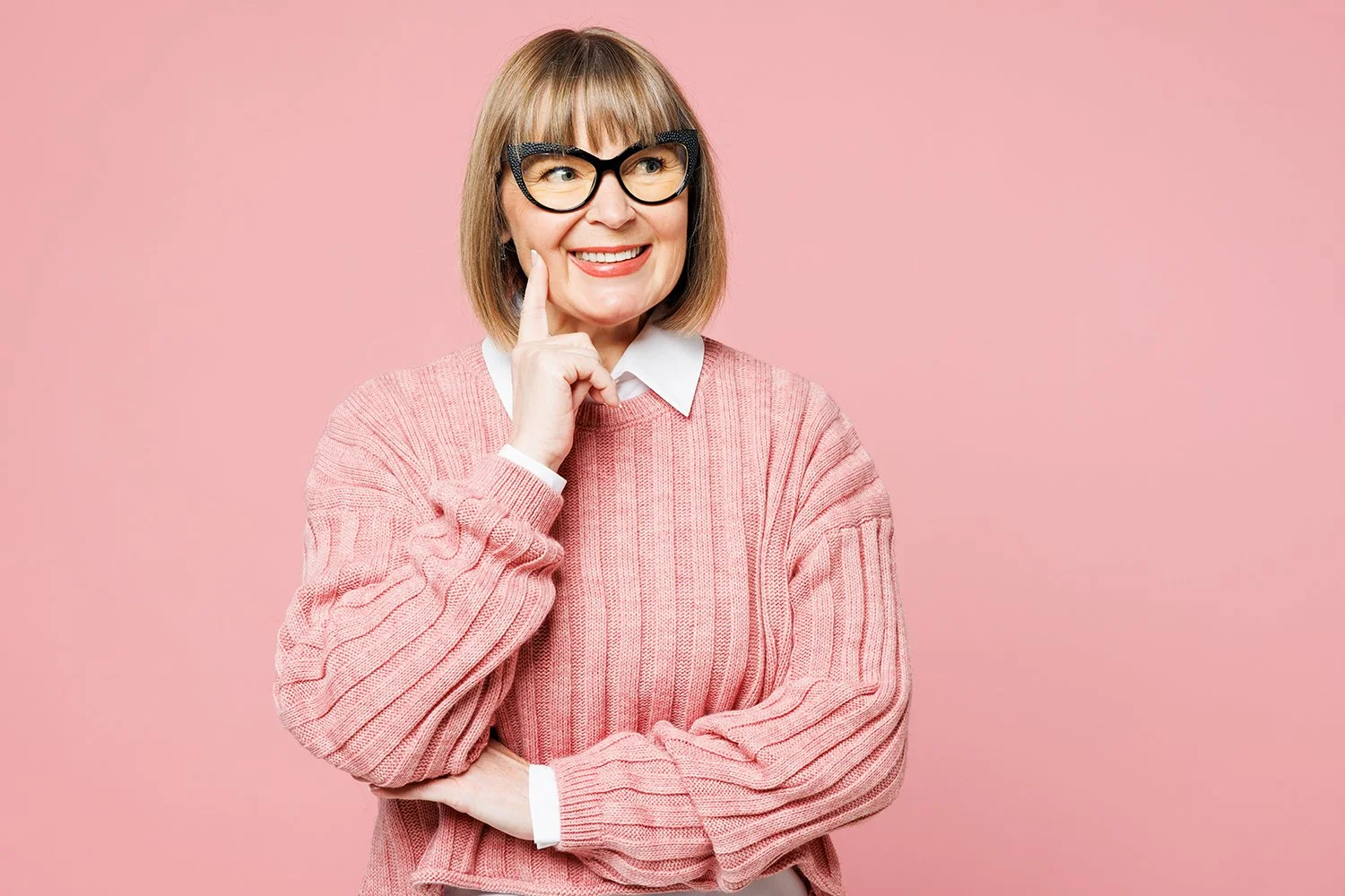 Senior woman in pink sweater with black glasses holding her finger to her dimple