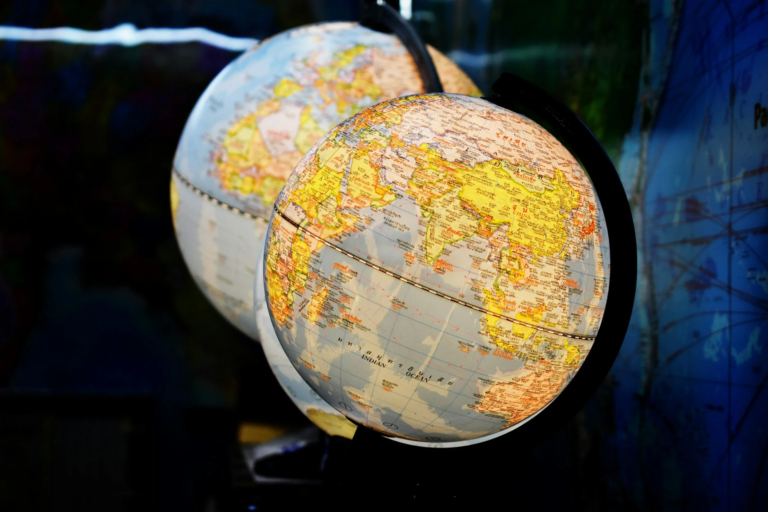 Two illuminated globes, one in front of the other, showing a world map with continents and countries outlined in yellow and orange.