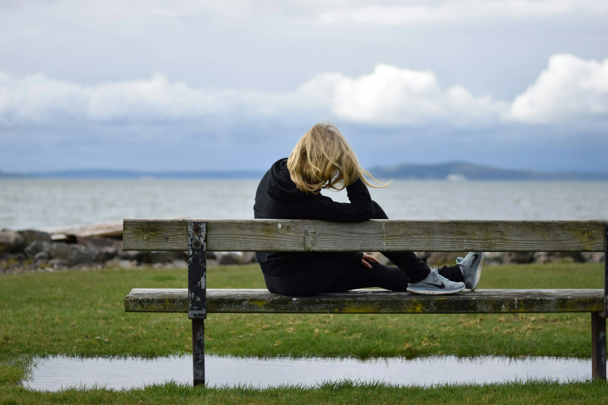 Photograph of a woman sitting on a bench looking out at the ocean.