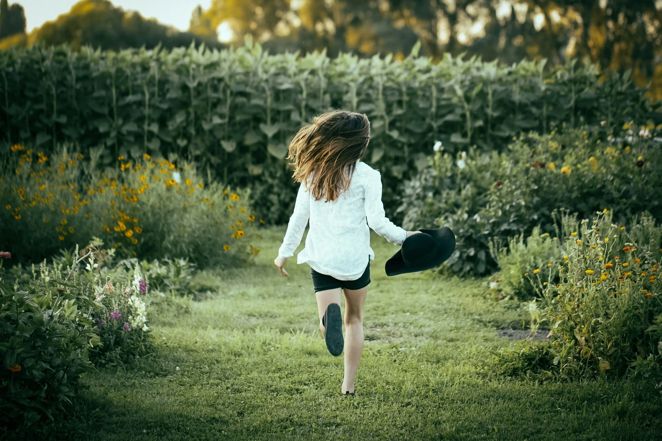 Image of a woman running in a garden, her back is turned away.