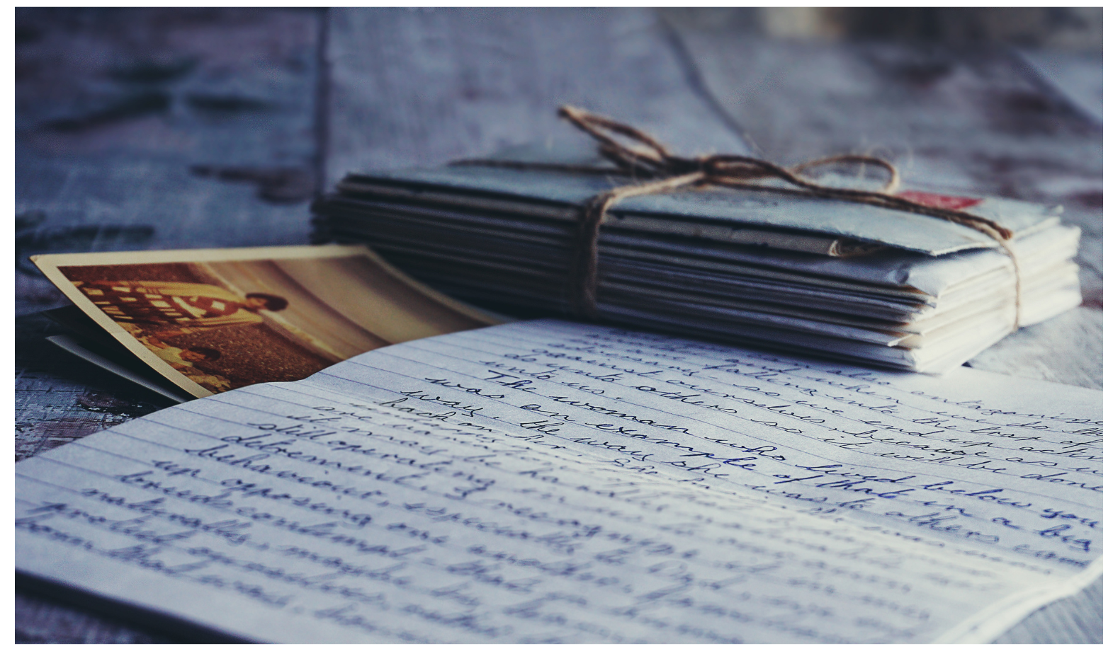 A stack of vintage letters tied with string, a handwritten letter, and a vintage photograph on a table.
