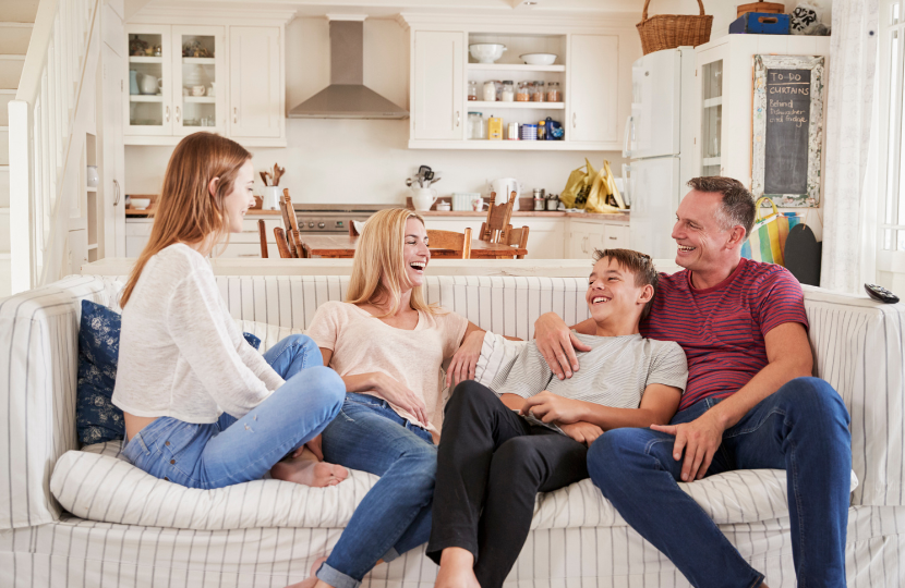Family of four sitting on a striped couch in a bright kitchen, laughing and enjoying each other's company.