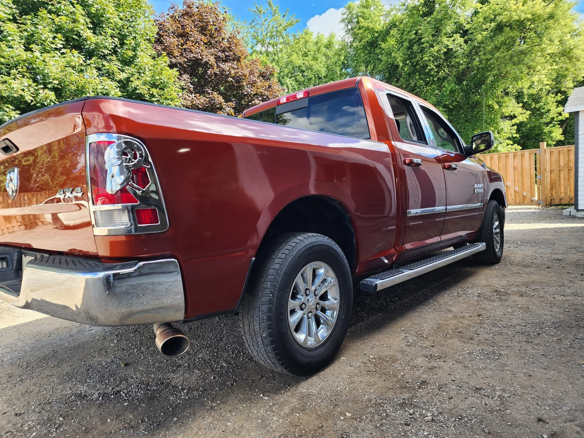 Red Ram 1500 pickup truck parked on a dirt lot with a background of trees and a wooden fence.