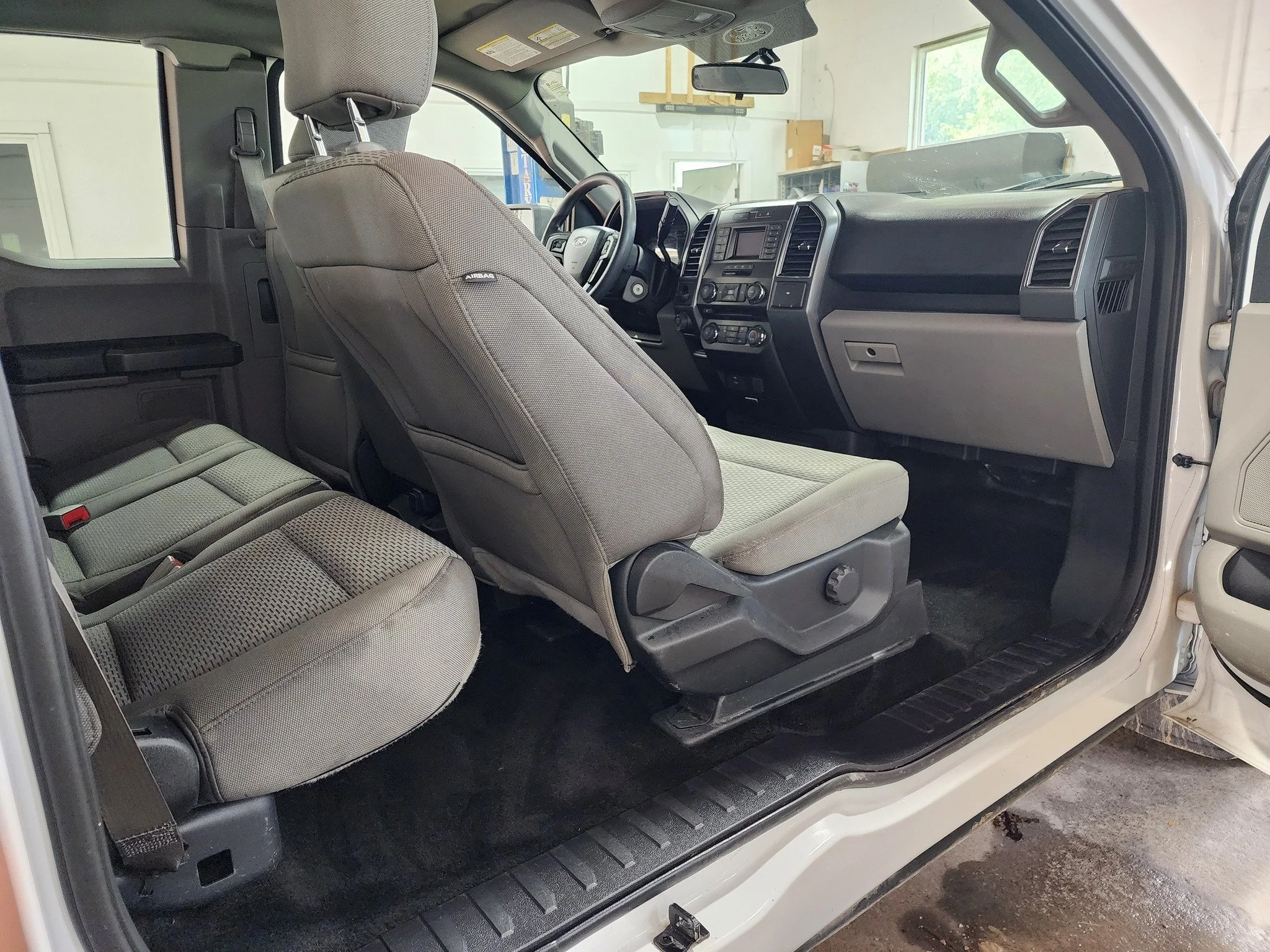 Interior of a vehicle showing the front seats, steering wheel, dashboard, and part of the backseat, with the driver's door open.