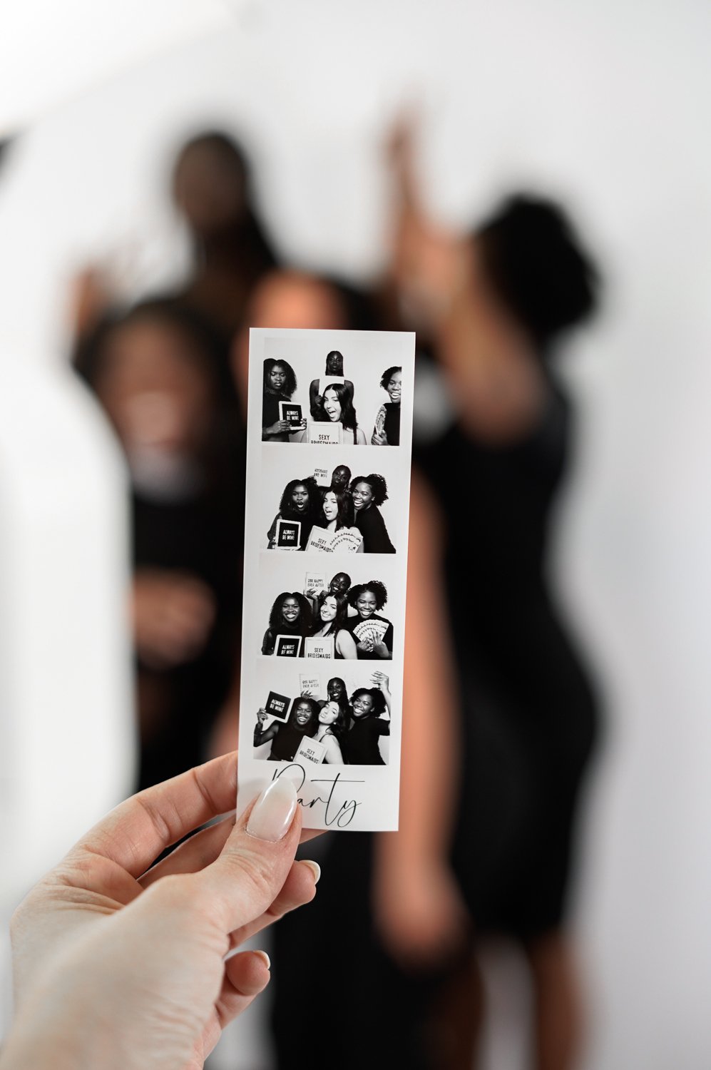 A photo booth strip showing four black-and-white pictures of women celebrating at a party, with one woman holding signs and making expressive faces.