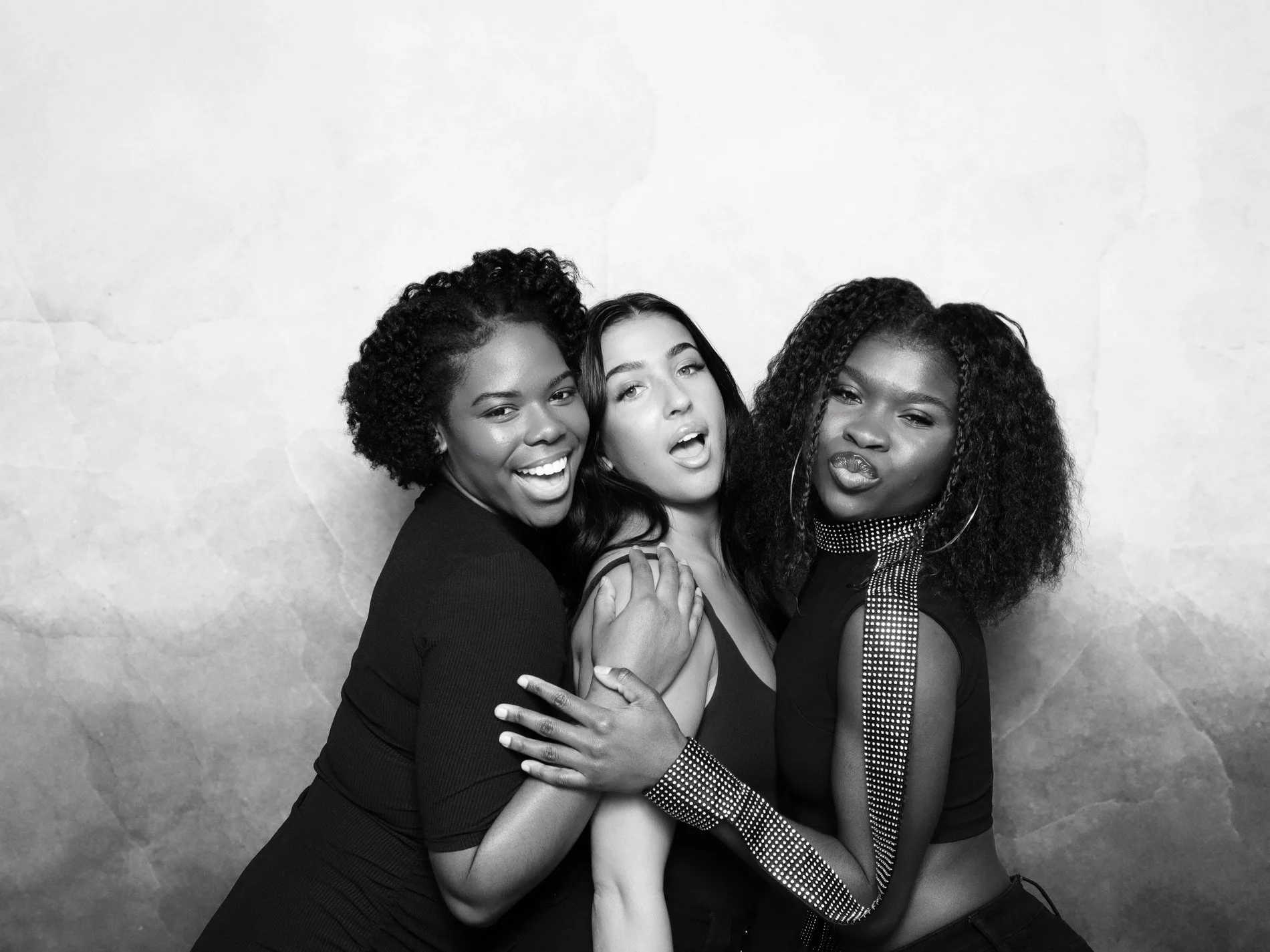 Three women posing together in black and white photo, smiling and making playful expressions.