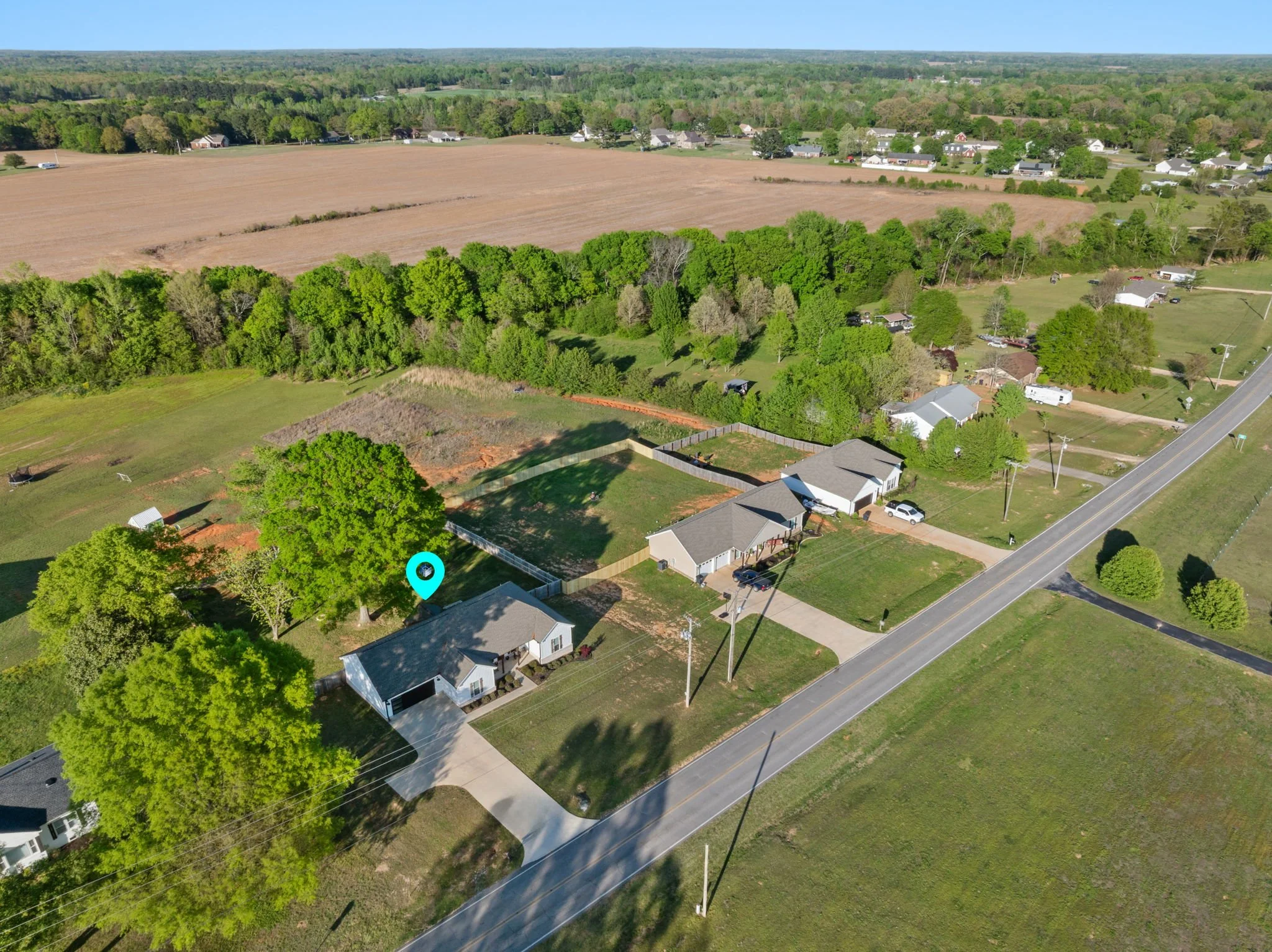 Aerial view of a suburban neighborhood with houses, trees, a road, and open fields.