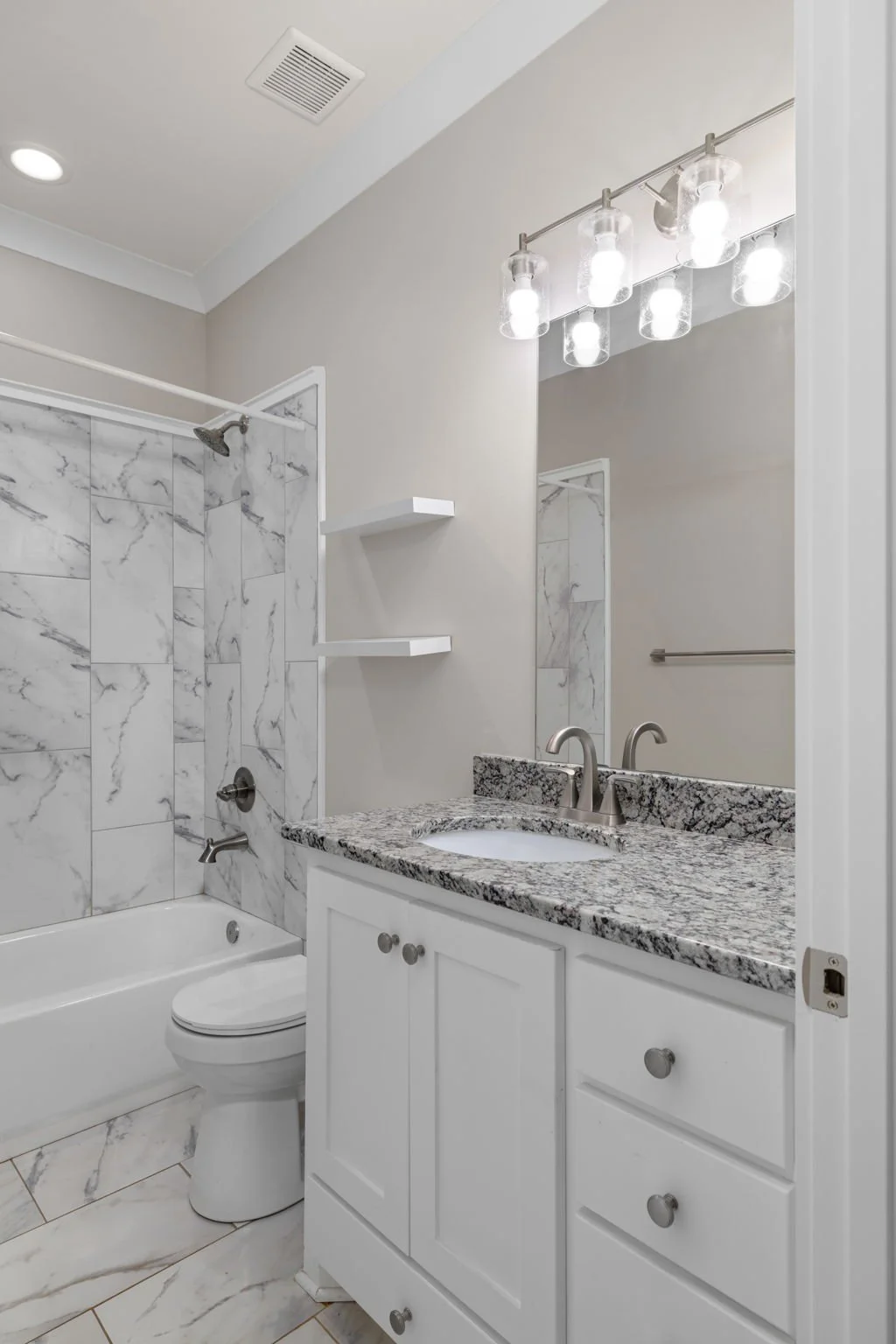 Bathroom with marble tile shower, white toilet, granite countertop vanity with sink, large mirror, and modern light fixture.