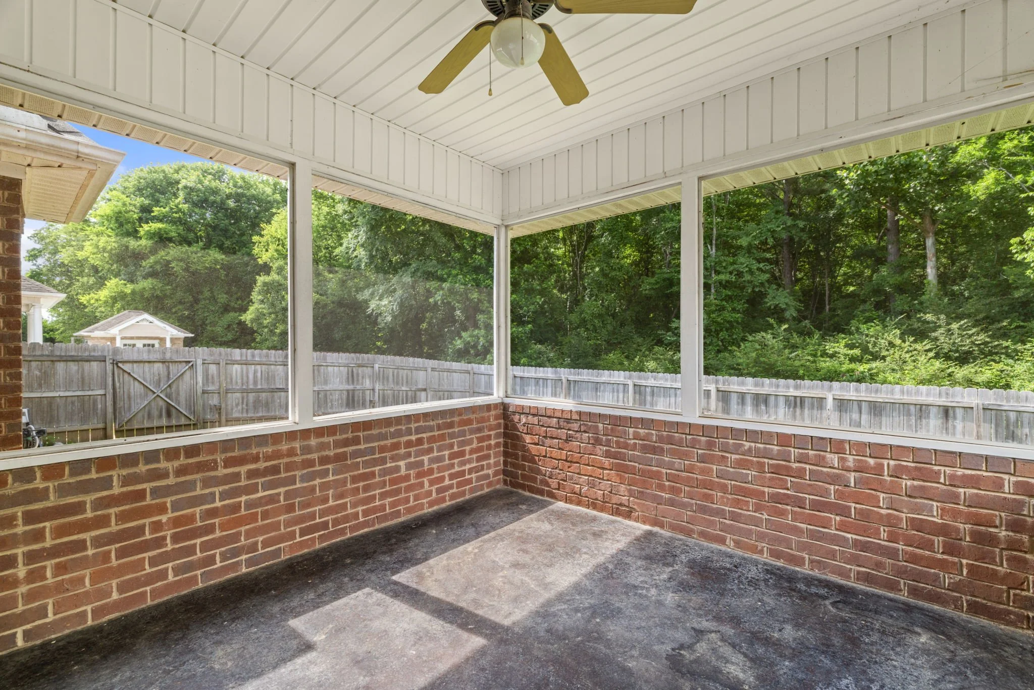 Covered porch with brick walls, a ceiling fan, a white ceiling, and a background view of green trees and neighboring houses.