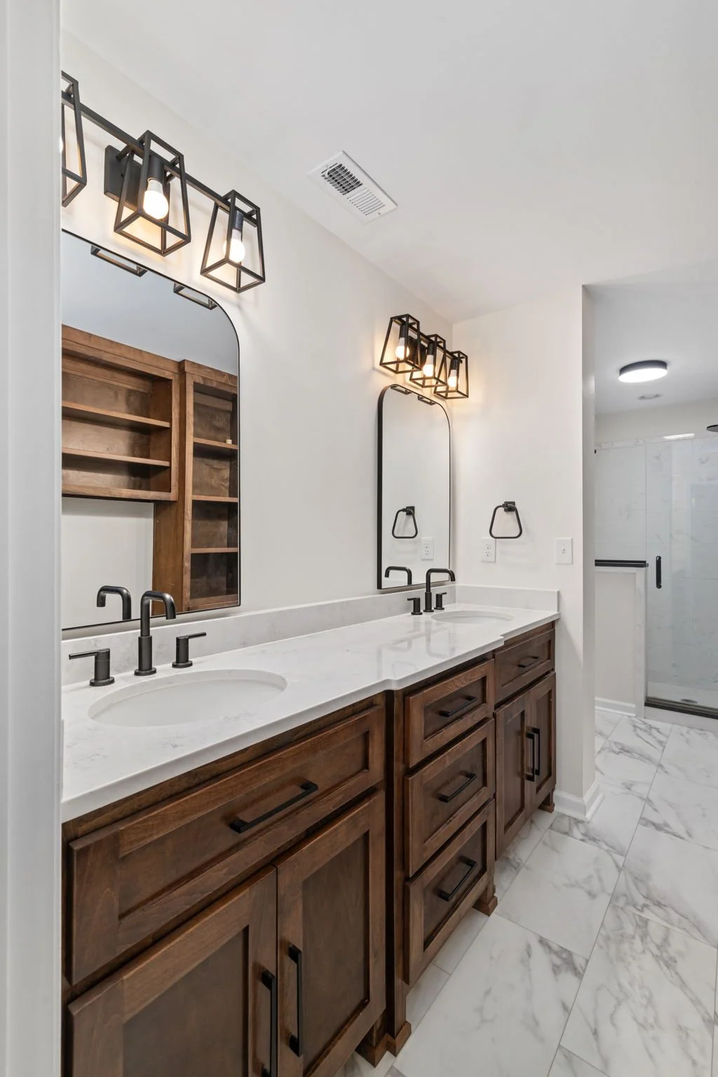 Bathroom with double vanity, wooden cabinetry, white marble countertop, black fixtures, rectangular mirrors with black frames, and modern light fixtures.