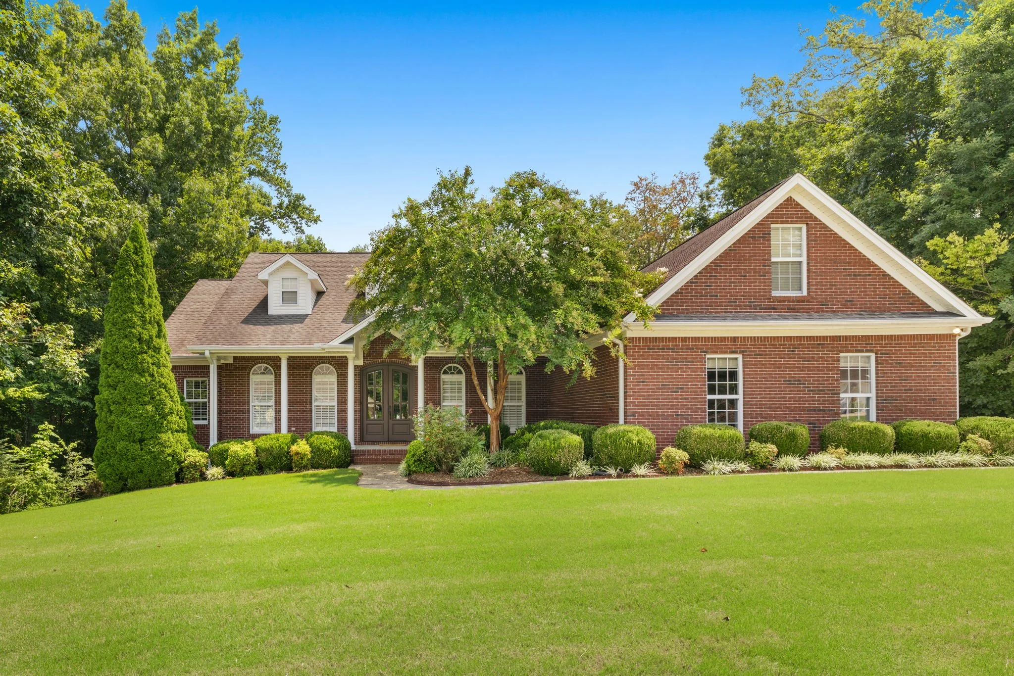 A brick house with a gable roof, surrounded by green trees and a well-maintained lawn.