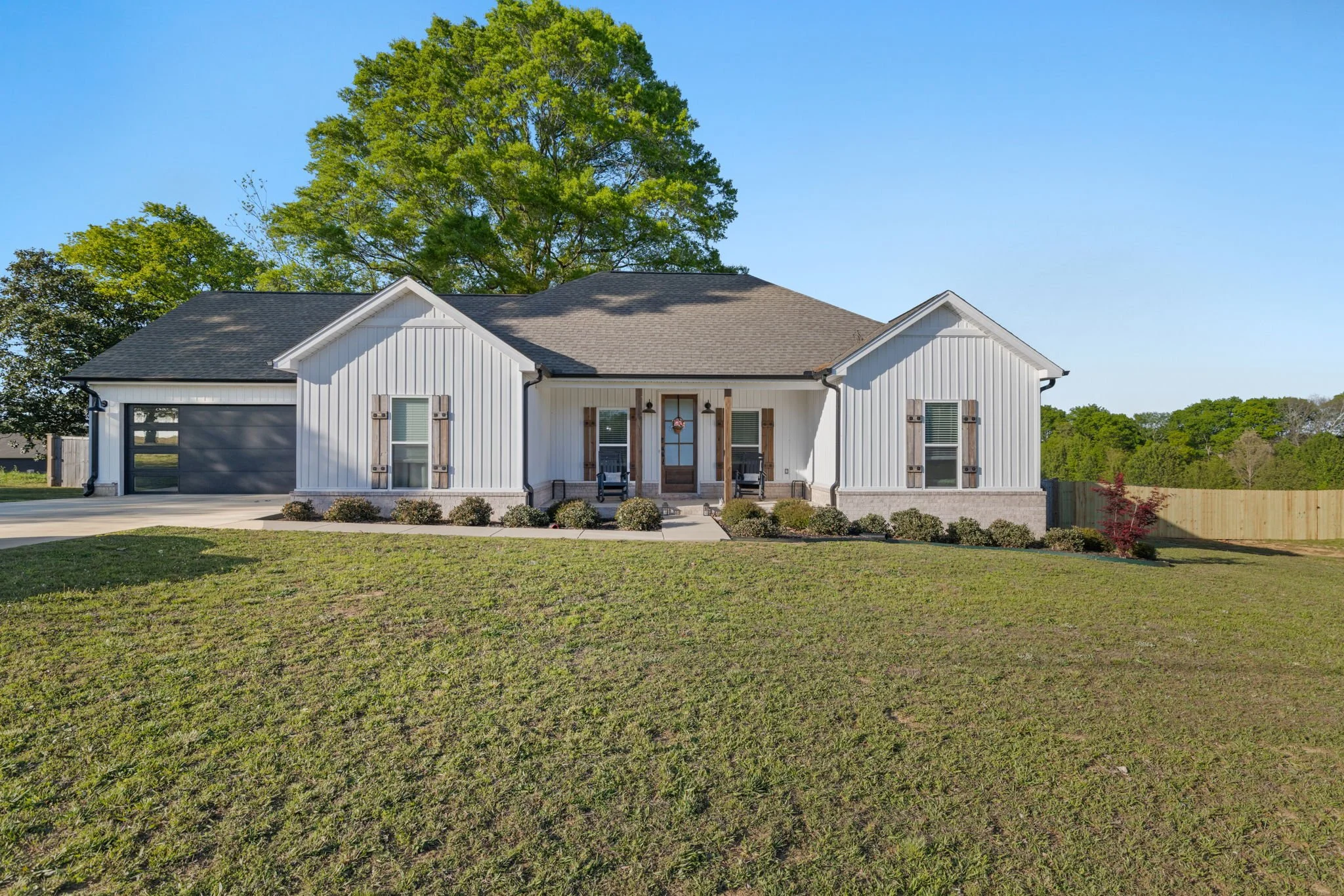 Front view of a modern white house with a dark gray garage door, a front porch with chairs, and a lush green lawn.