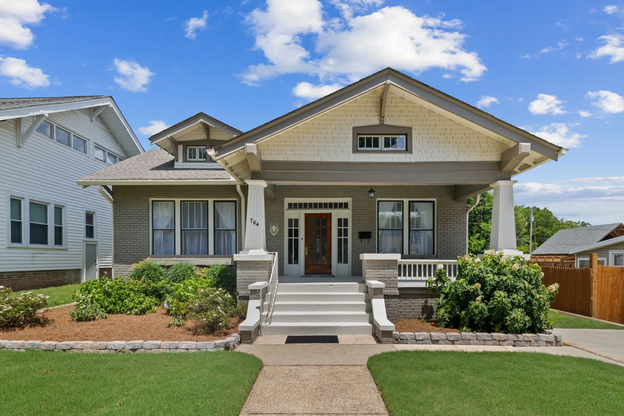 Front view of a house with a porch, steps, and a landscaped front yard, under a partly cloudy sky.
