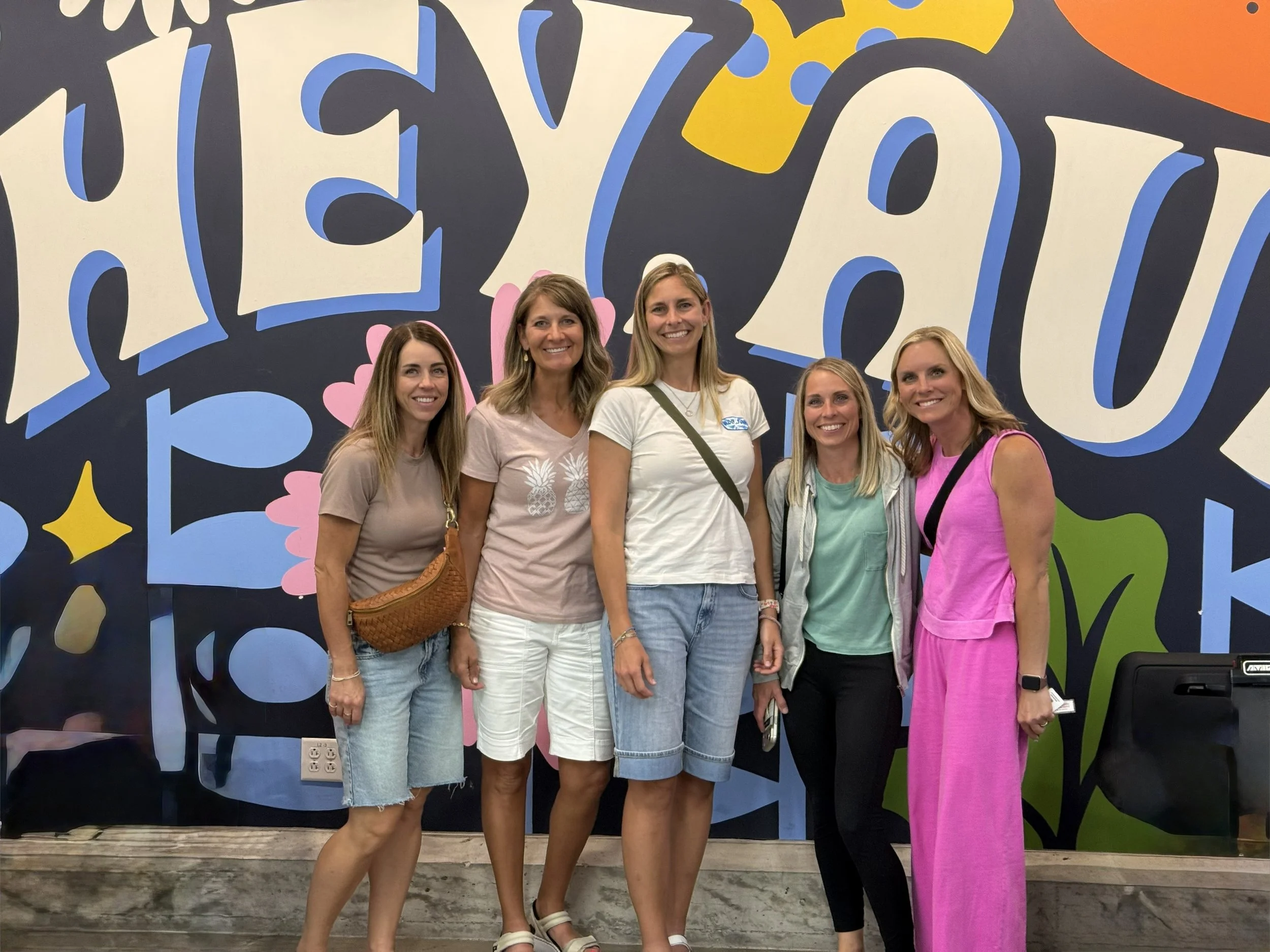 Five girlfriends posing for a picture in front of a mural