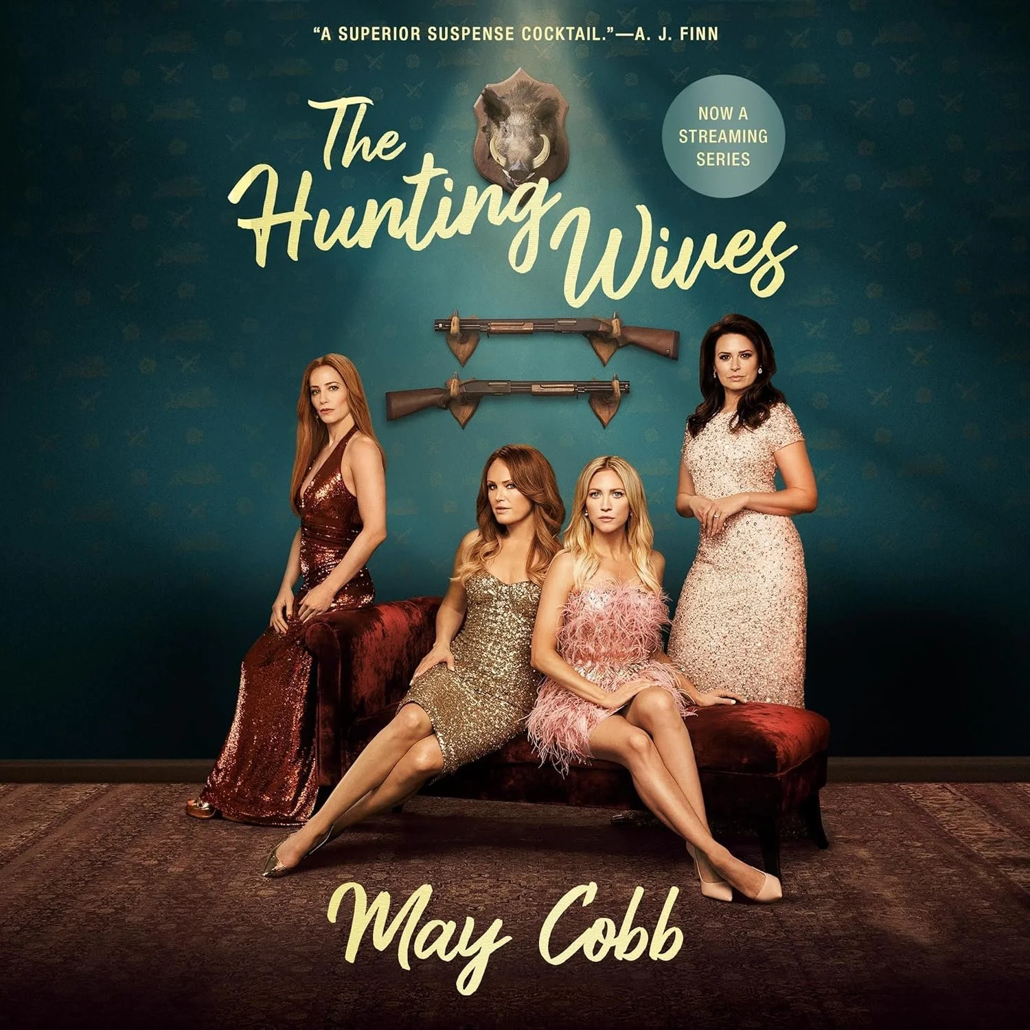 Promotional poster for the streaming series 'The Hunting Wives' featuring four women in glamorous dresses, two sitting on a velvet bench and two standing behind, with rifles mounted on the wall behind them. The background is teal with a wolf head and the title in large cursive. The writer's name, May Cobb, is at the bottom. A quote from A. J. Finn is at the top.