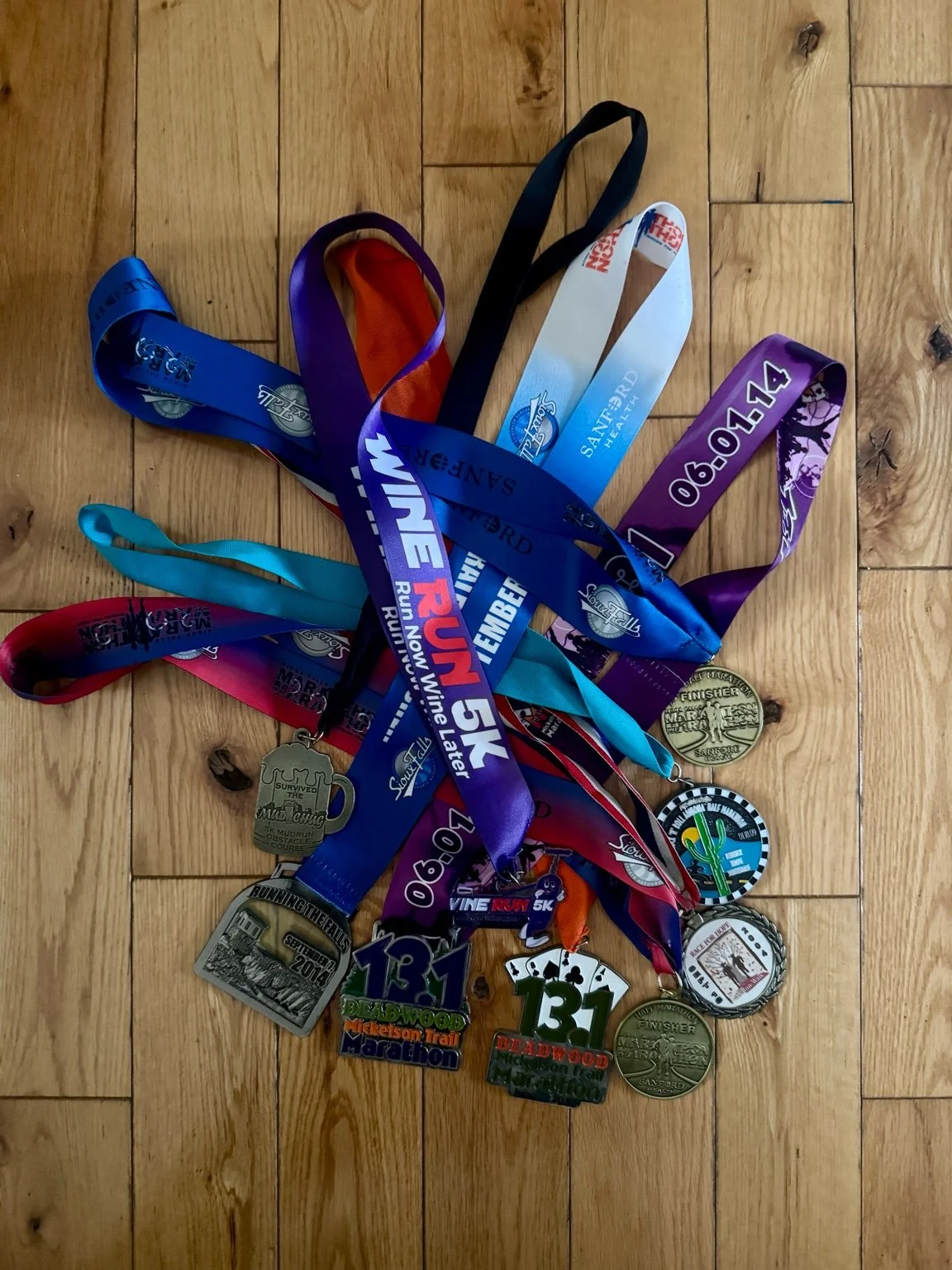 A collection of marathon and running medals with colorful ribbons laid out on a wooden floor.