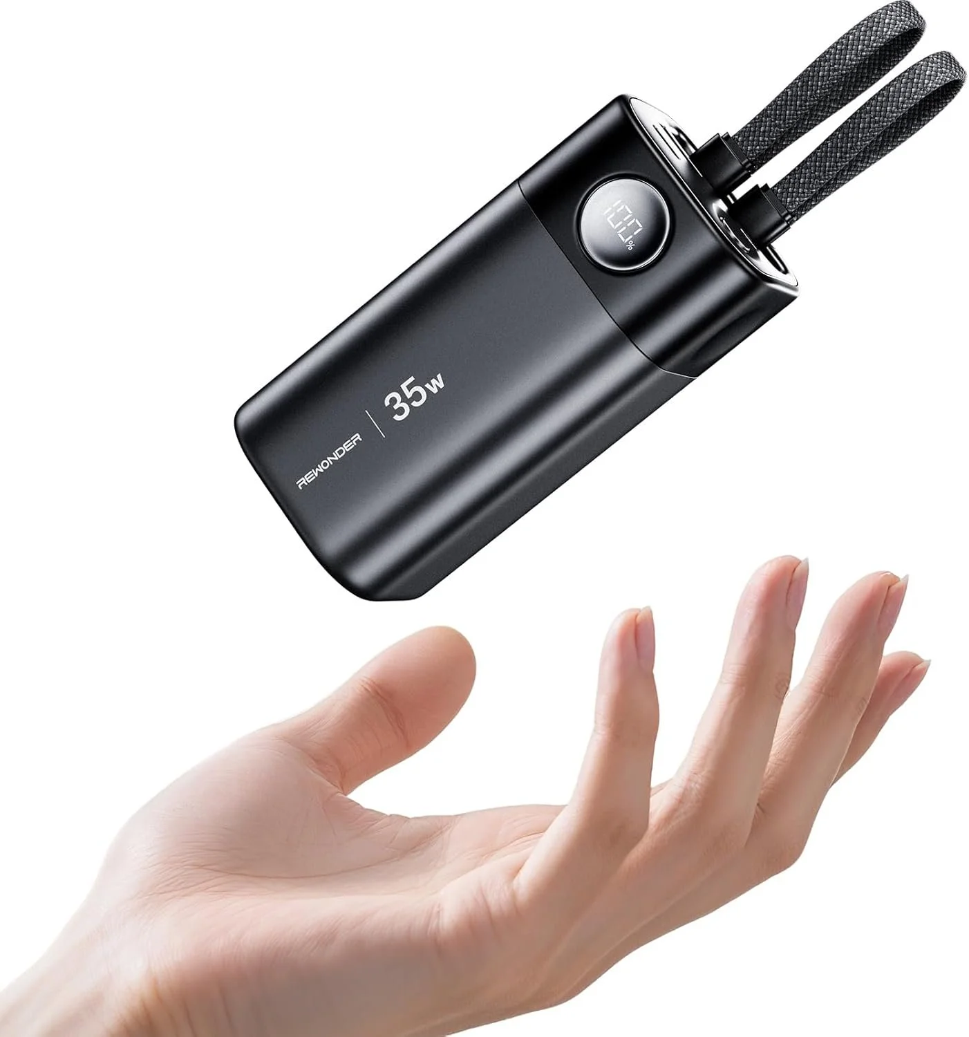 A black portable 35-watt power bank with a digital display and two braided charging cables floating above a person's open hand.