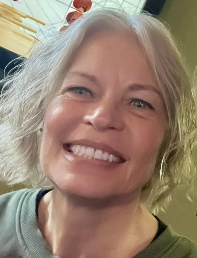 Close-up of a smiling woman with short, wavy, gray hair, wearing a light green shirt.