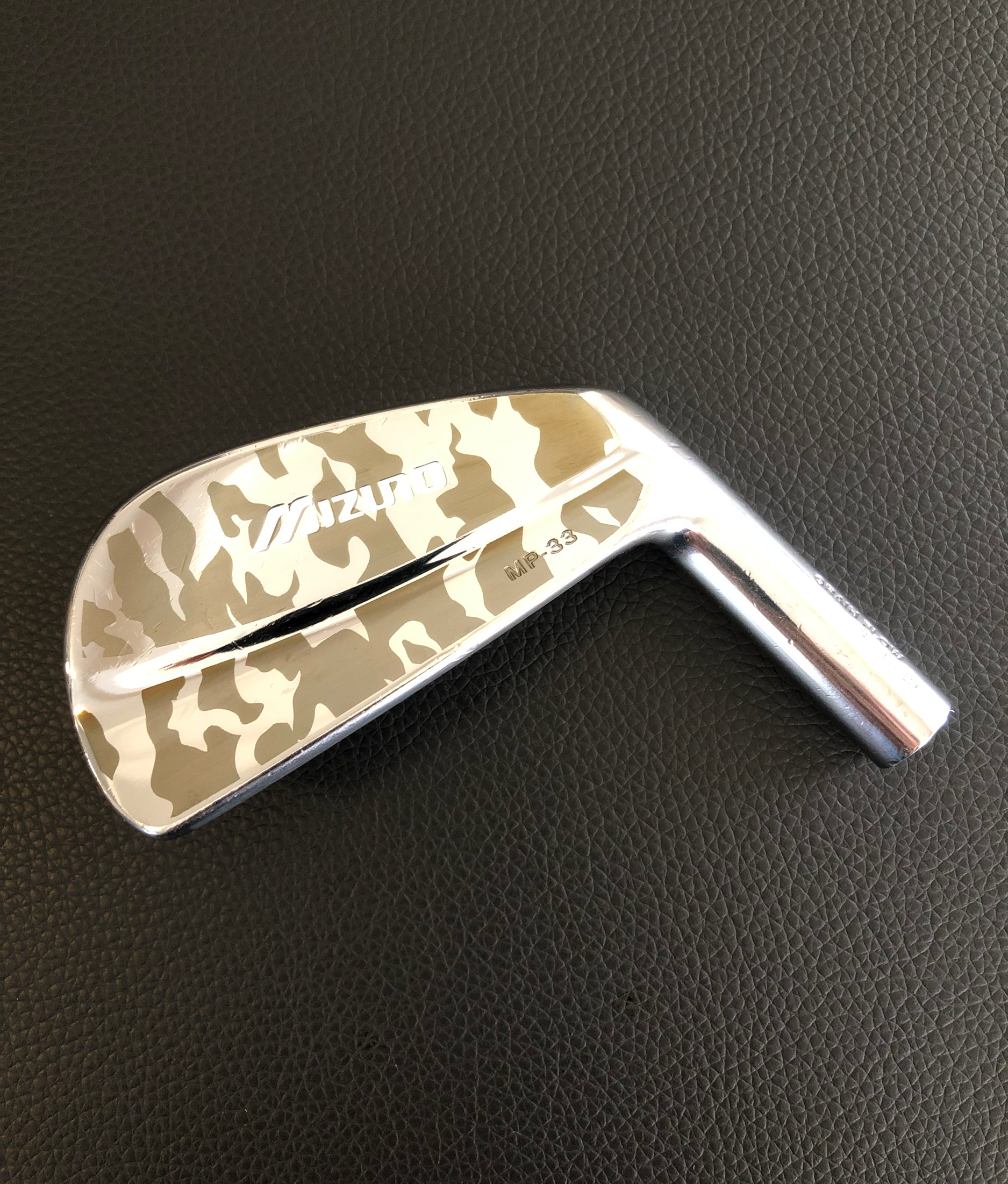Golfclub mit Camouflage-Design und Markierung 'Mizuno', liegt auf schwarzem Leder
