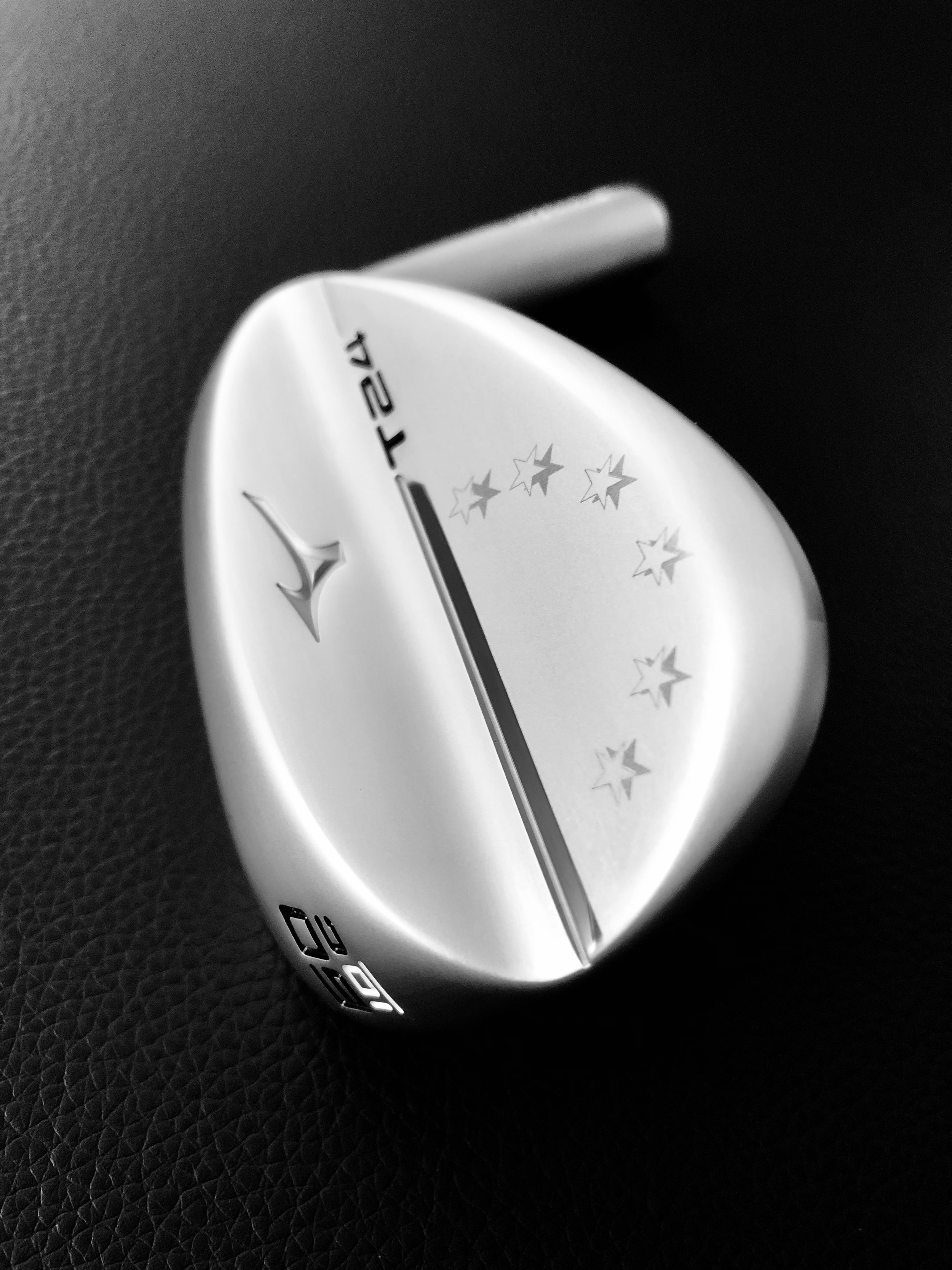 Golfschläger mit silberner Oberfläche, Markierung und Sterne-Design, liegt auf schwarzer Oberfläche.