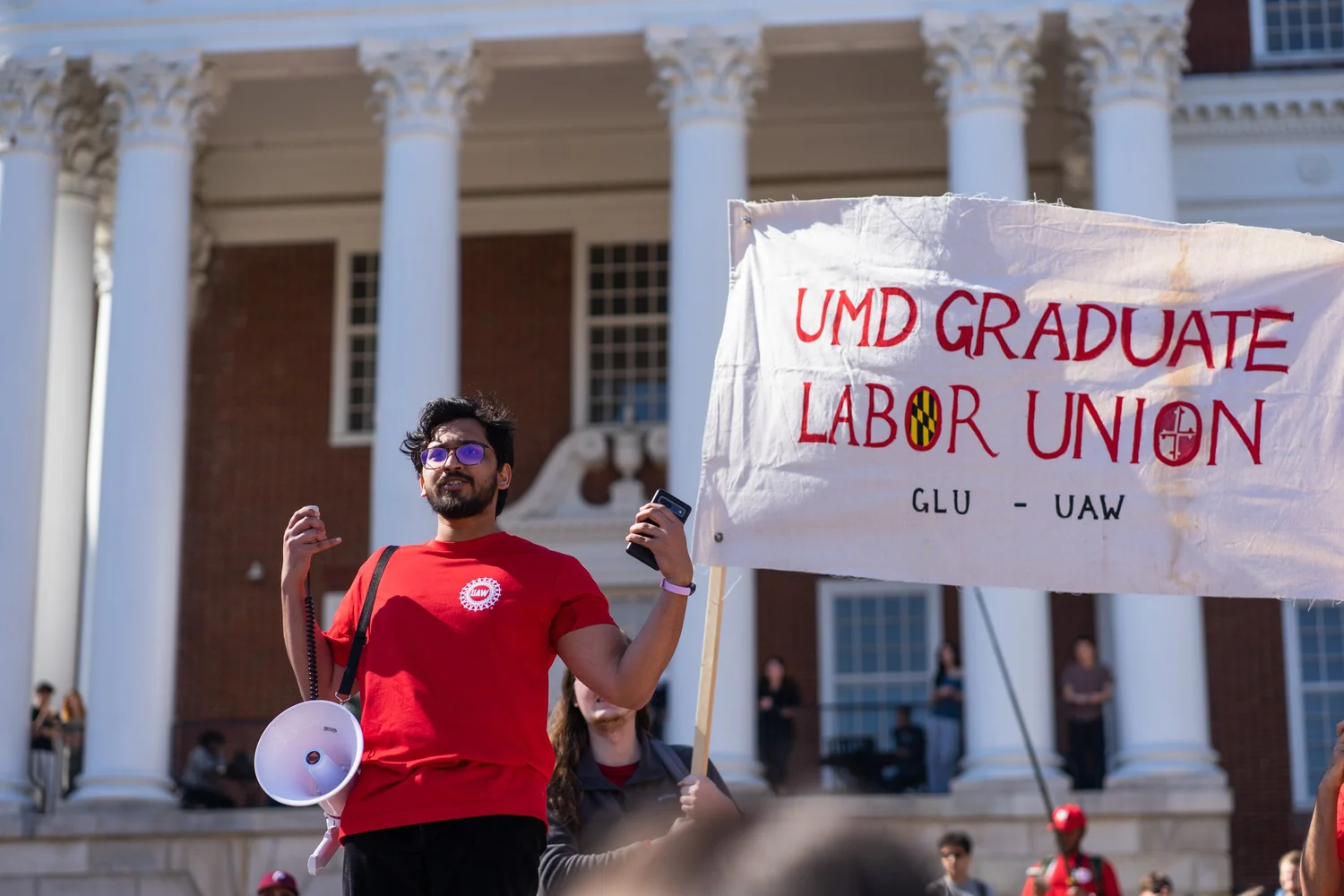 A UMD Graduate Labor Union member speaking beside a GLU-UAW banner
