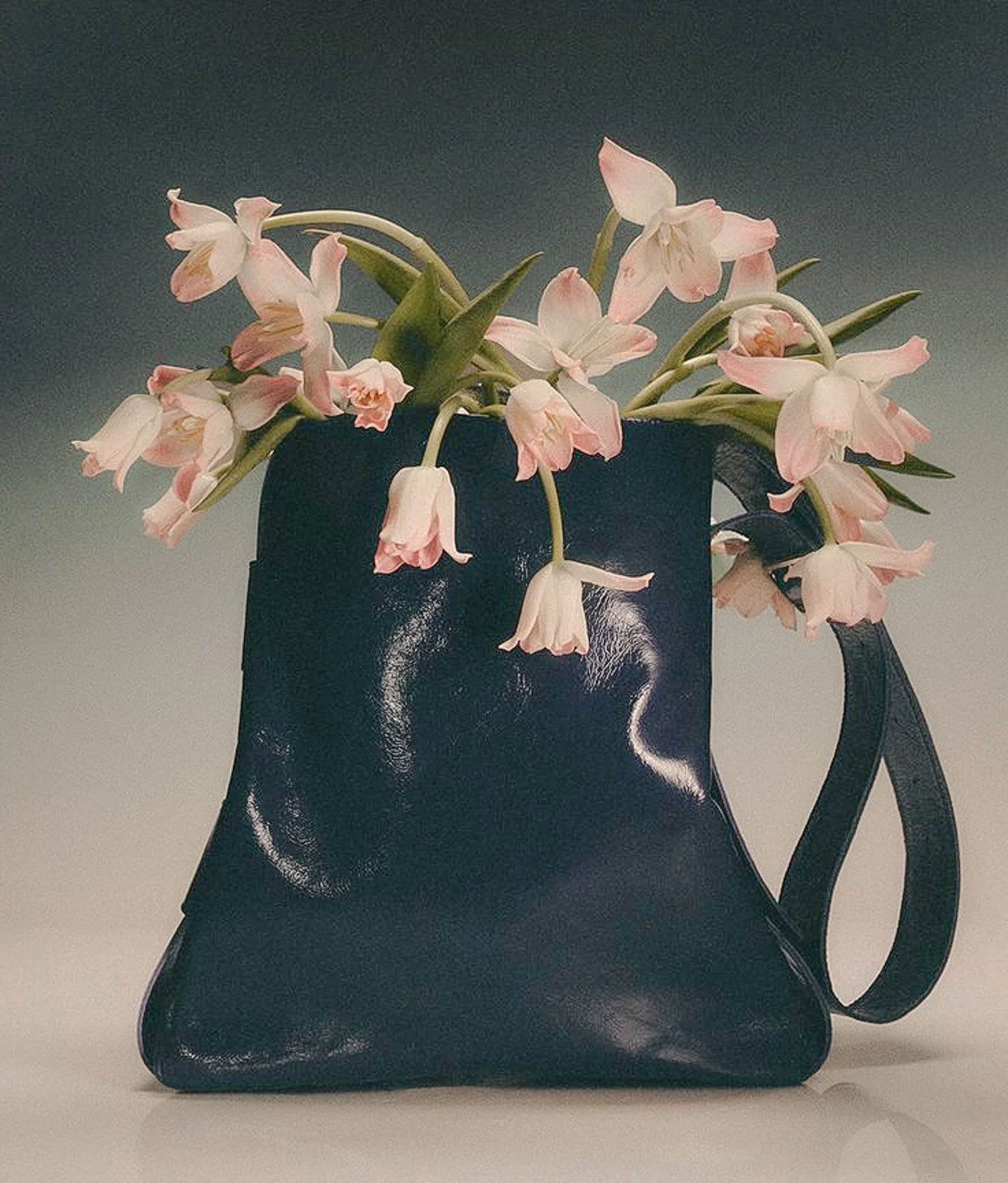 A black handbag filled with pink and white flowers with droplets of water on the surface.