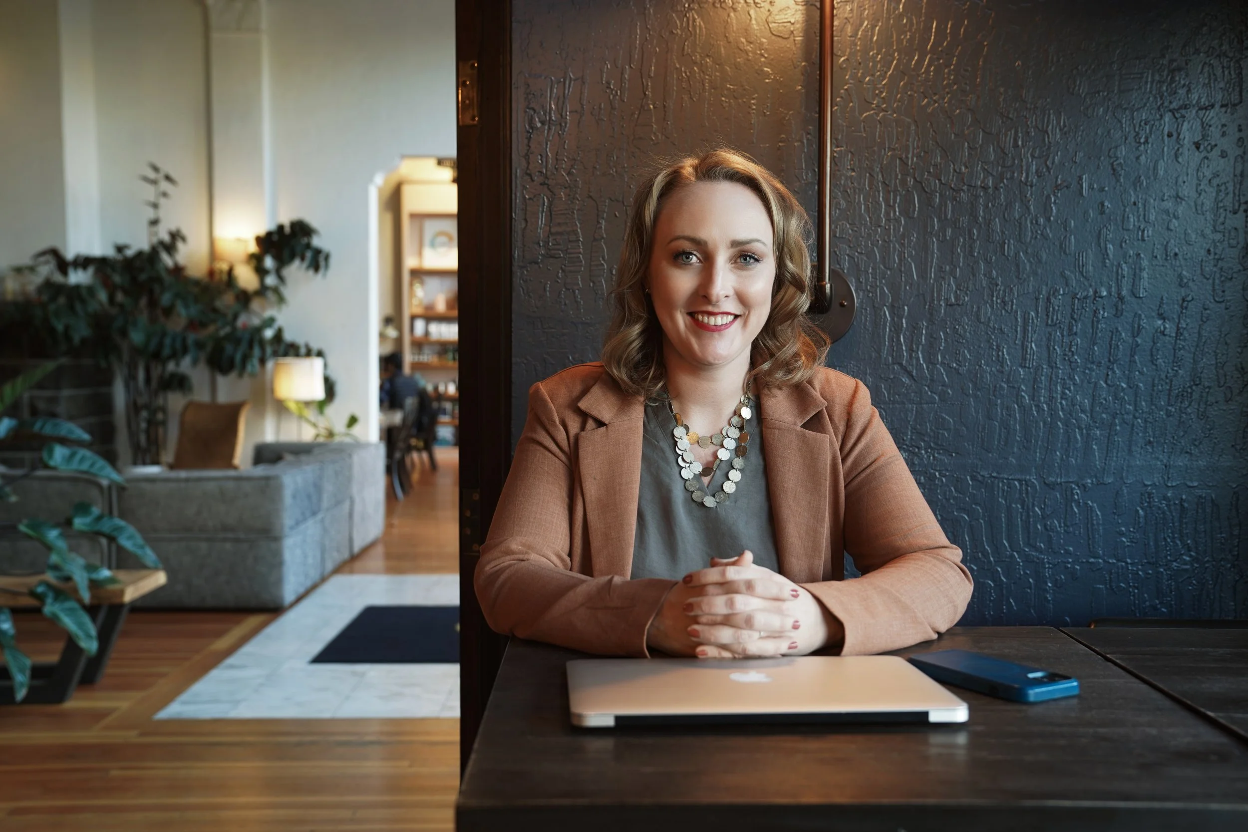 Diana Pullen, Redmond Oregon real estate broker in Central Oregon sitting at a laptop on a dark wooden table in a cozy, modern cafe or workspace.