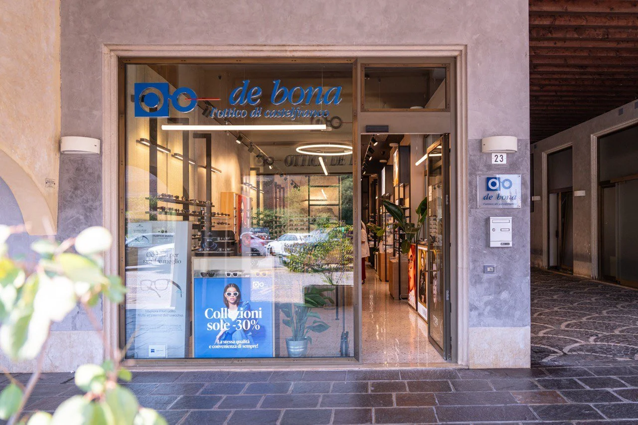 Vetrina di un negozio con insegna 'de bona ottico di castelfranco' e poster pubblicitario per sconti del 30% su occhiali.