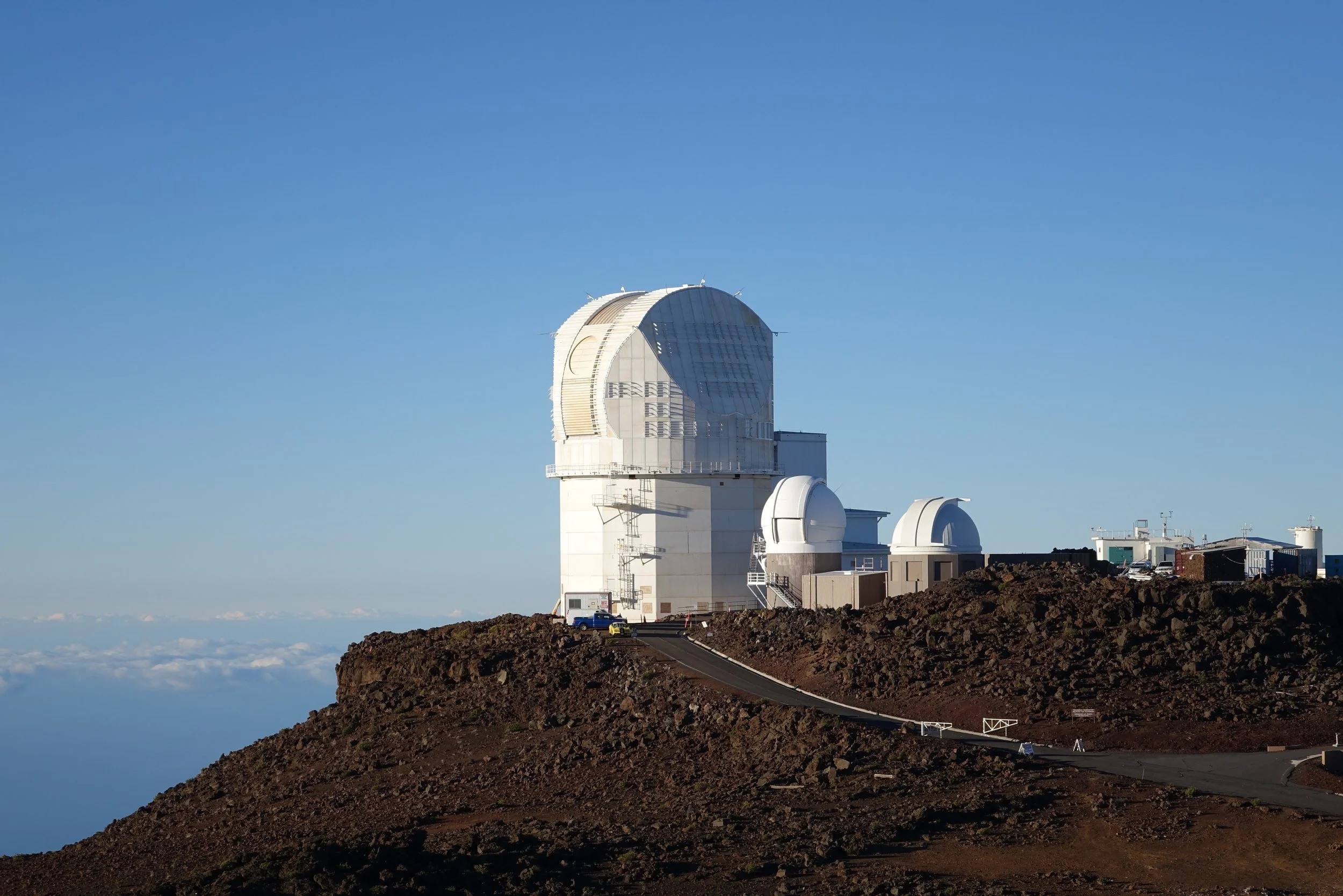 The Mauna Kea Observatory on a clear day, showing a large white telescope dome on a mountain with a dirt road leading up to it.
