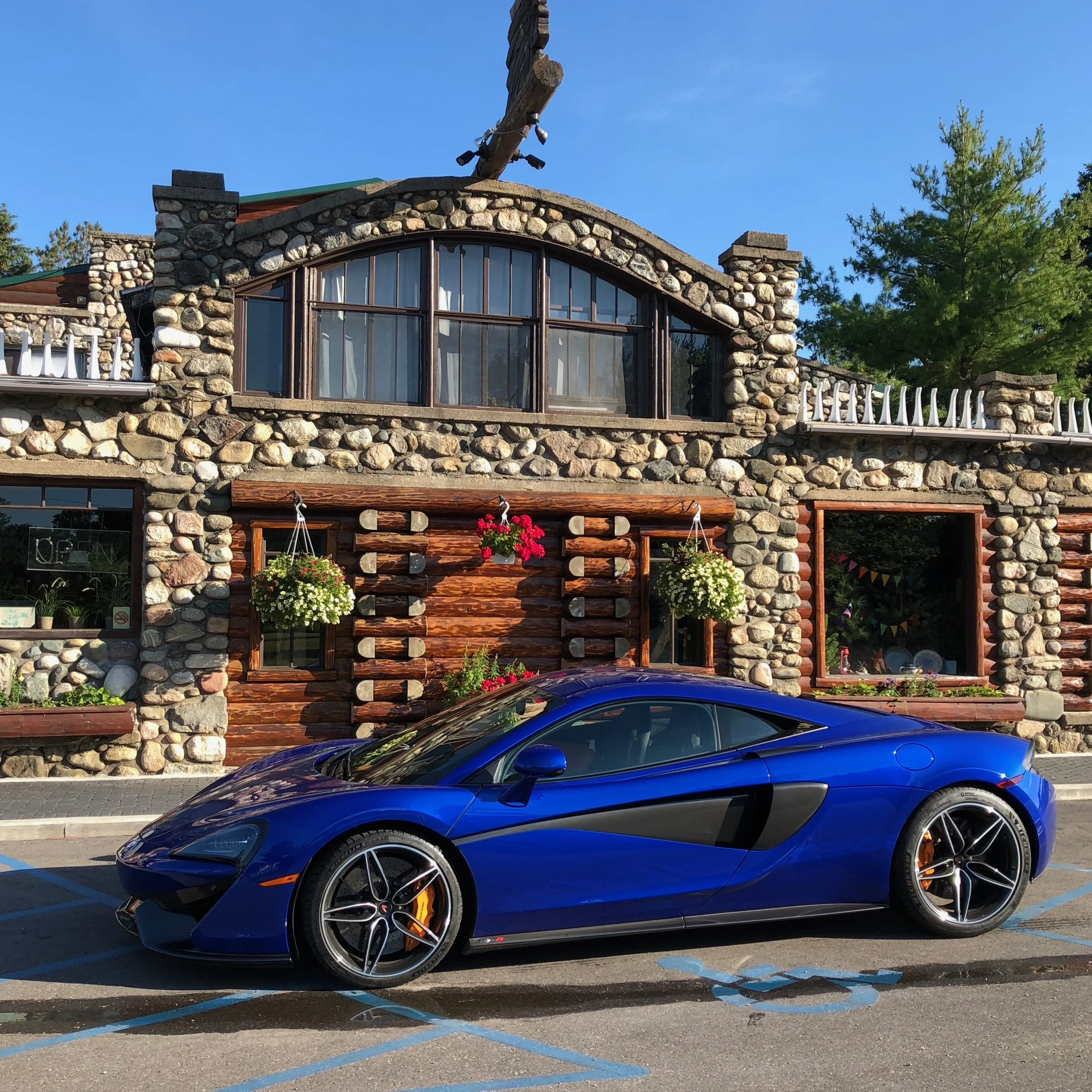 Blue sports car parked in a handicapped space in front of a rustic stone and wood building with hanging flower baskets and a large window