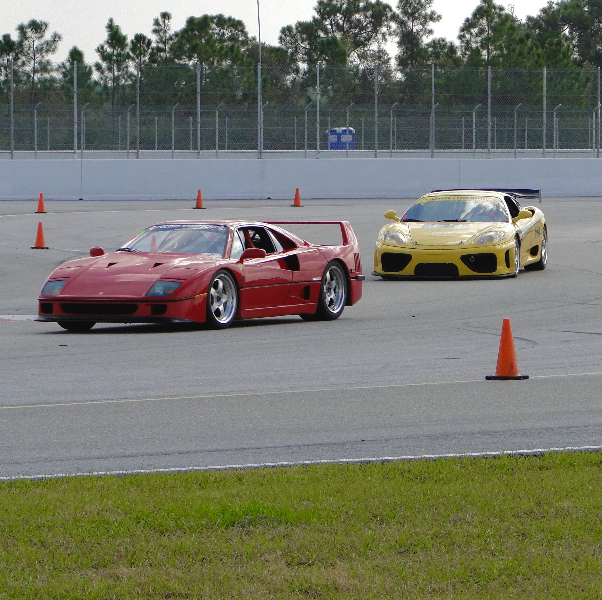 Two racing cars on a track with orange cones, one red Ferrari and one yellow race car, during a drifting event.