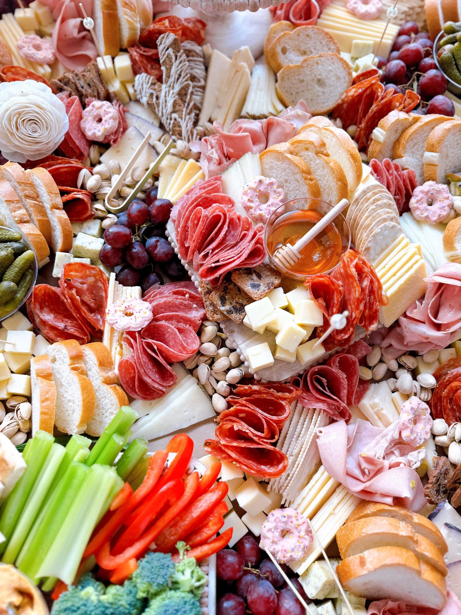 A charcuterie board with a variety of cheeses, sliced bread, grapes, cured meats, vegetables, and small donuts.