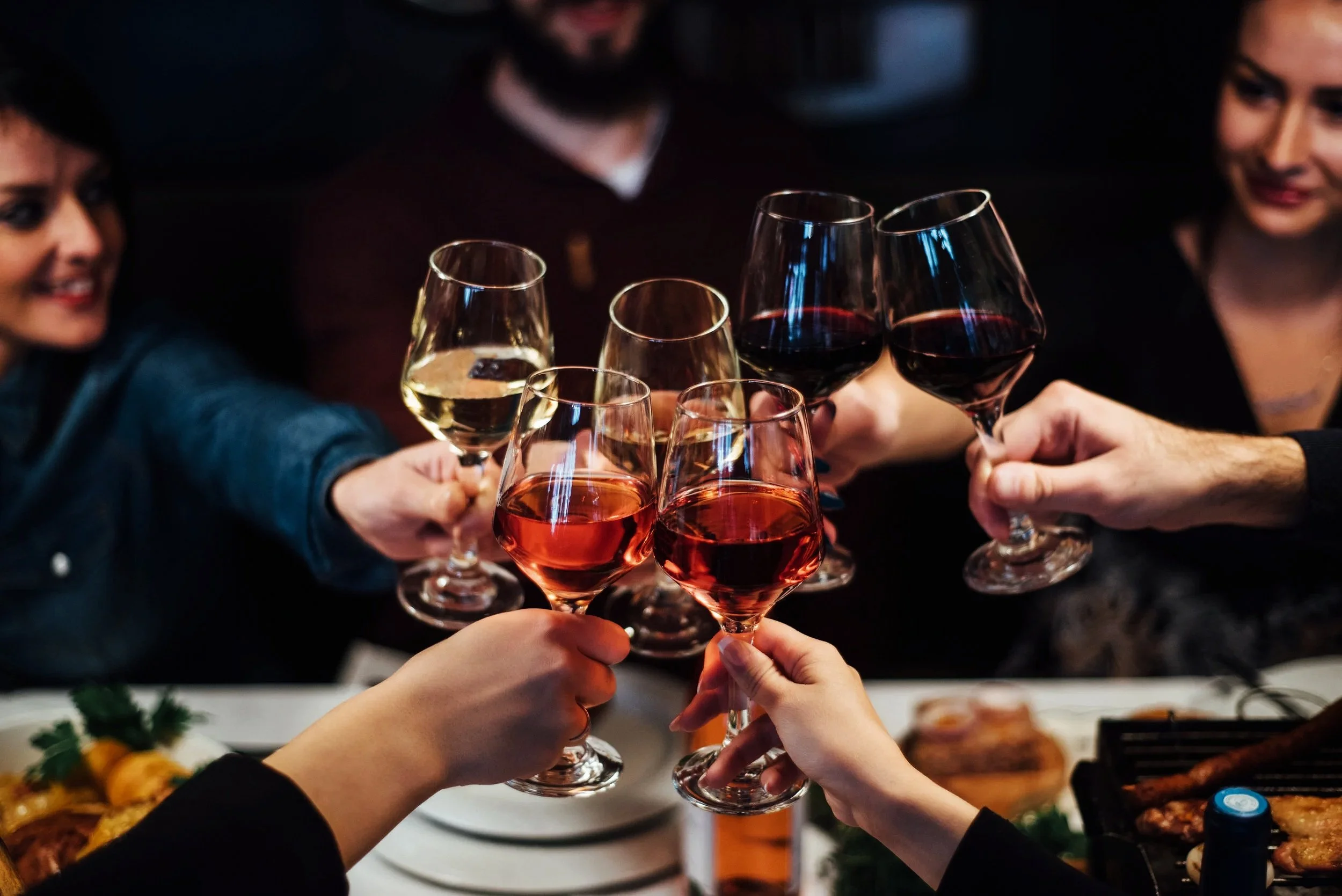 Group of people clinking wine glasses filled with red, white, and rosé wine during a social gathering.
